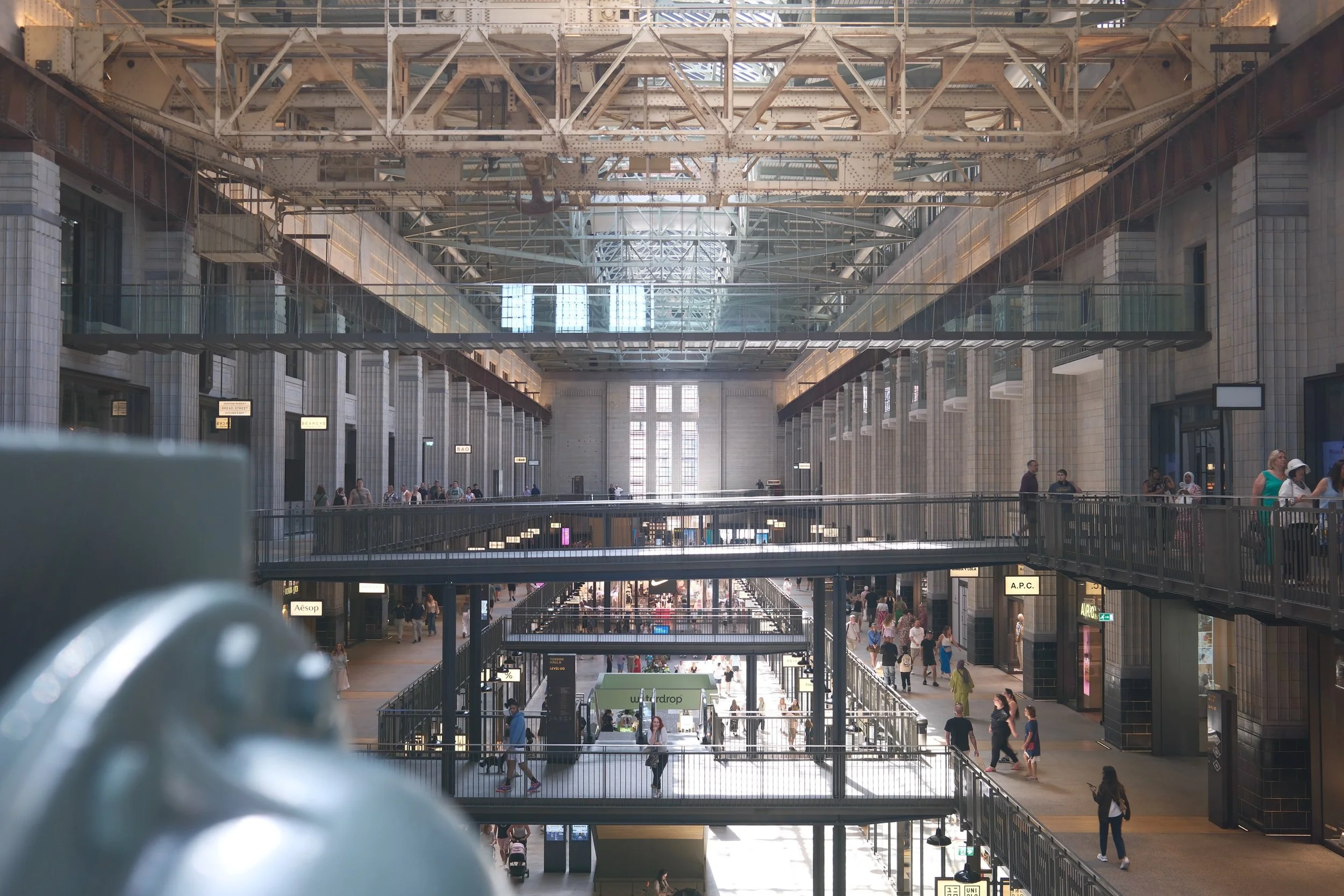 Interior of a large train station with multiple levels, glass bridges, and people walking around.