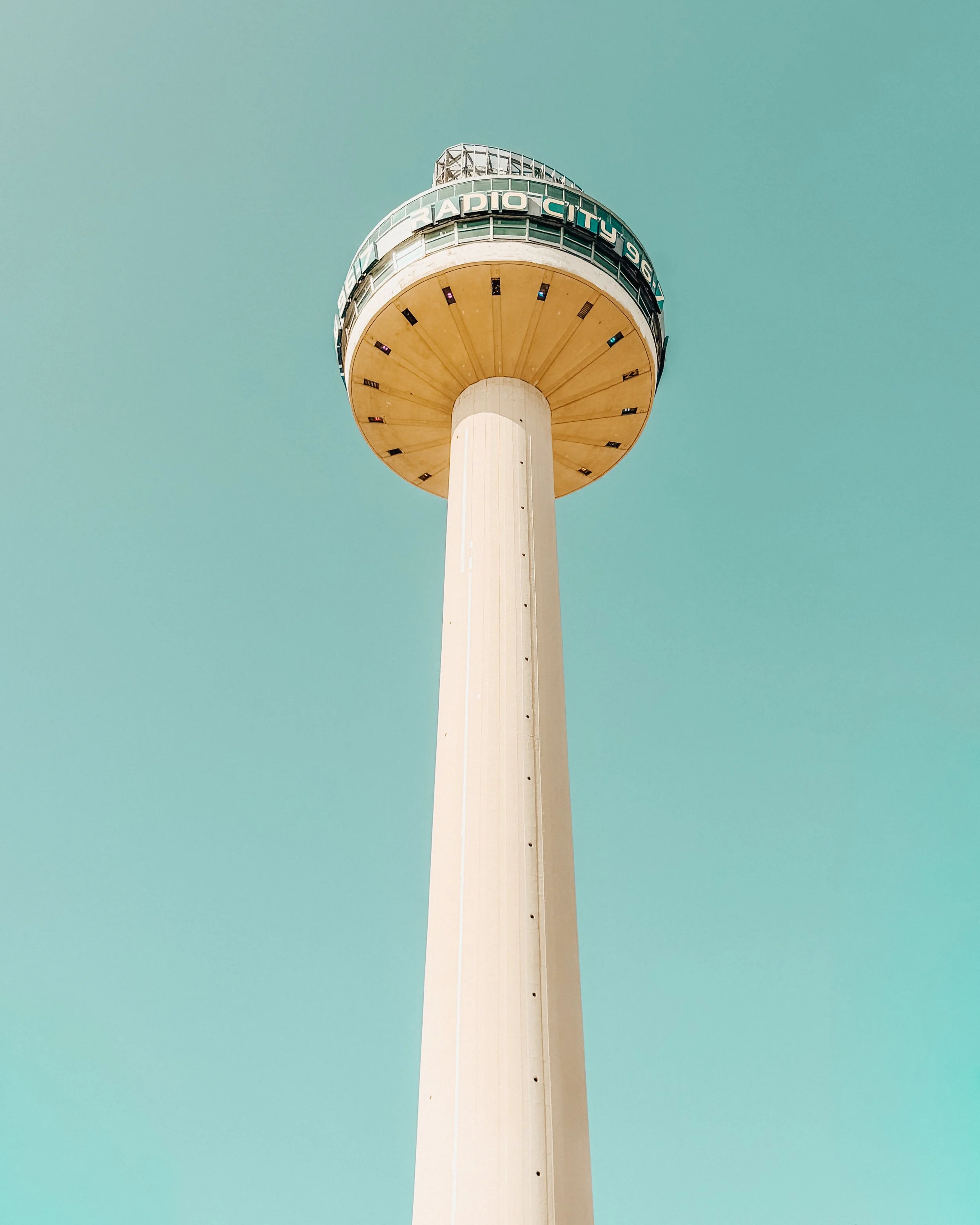A tall observation tower with a rounded top section and a white cylindrical base, set against a clear blue sky.