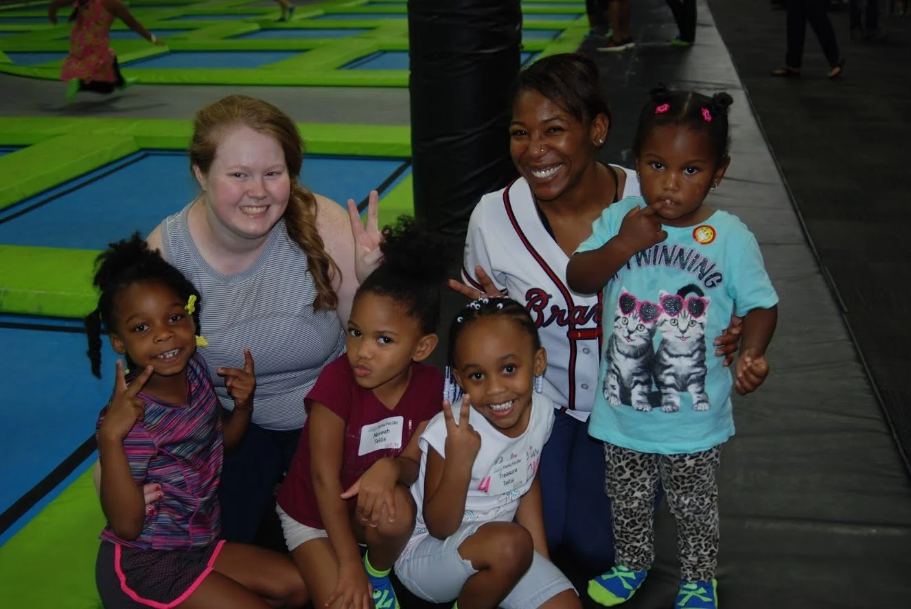 Group of children and a woman at an indoor trampoline park, smiling and posing for the photo.