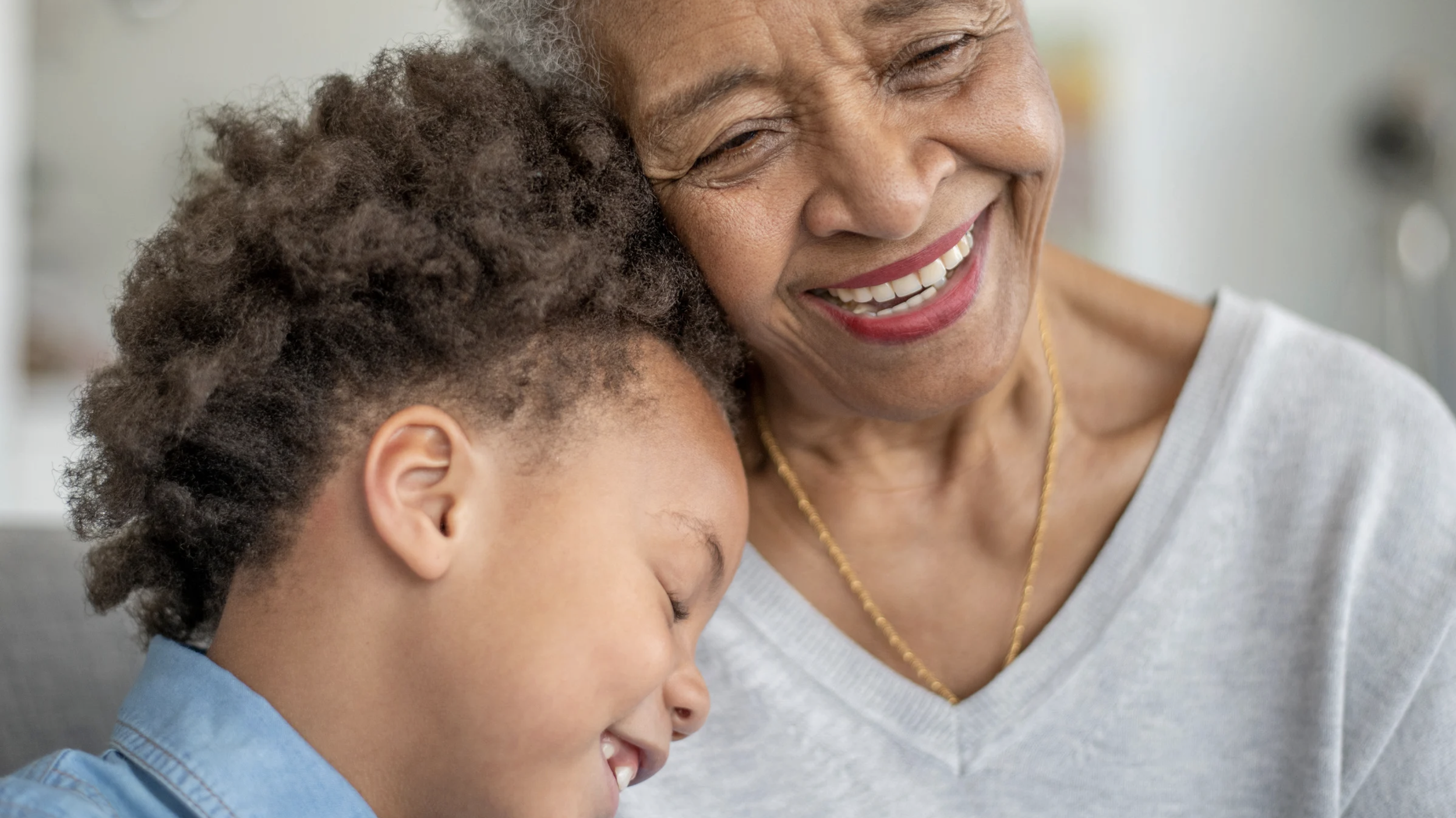 A close-up of a smiling elderly woman and a young boy hugging, both with their eyes closed.