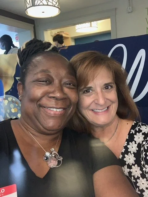 Two women posing for a selfie, smiling, in an indoor setting.