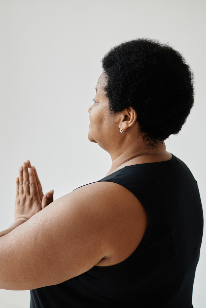 Side view of a woman with short curly black hair wearing a black sleeveless top, holding her hands in a prayer position.