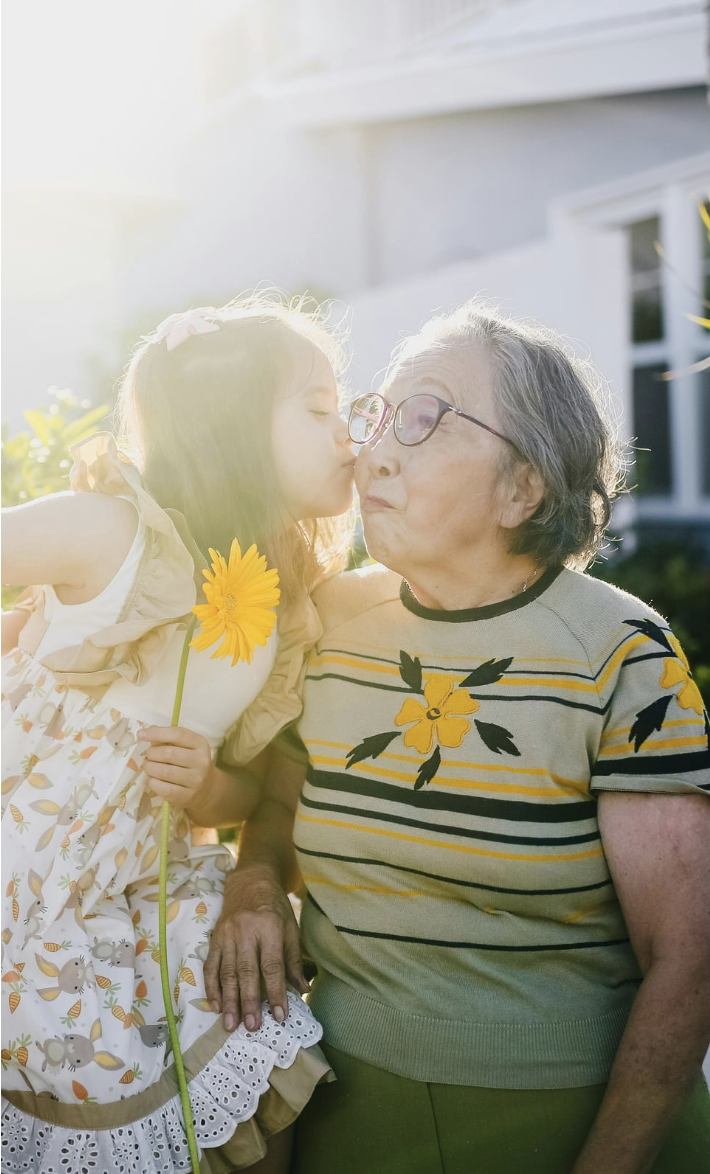 A young girl giving an elder woman a kiss on the cheek outdoors on a sunny day.
