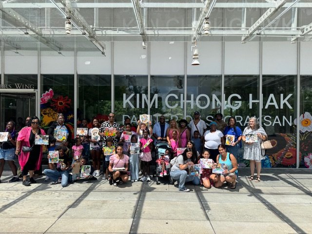 Group of people standing and sitting outside a building with large glass windows, holding flyers or posters, in front of Kim Chong Hak restaurant.