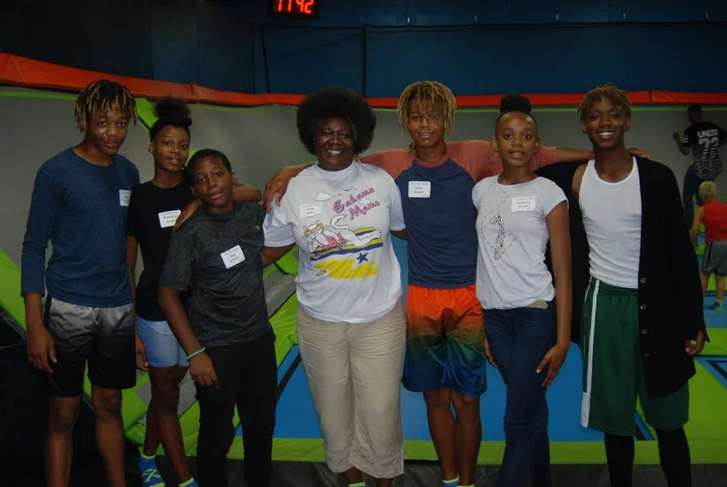 Group of seven kids and one adult woman posing together at indoor trampoline park