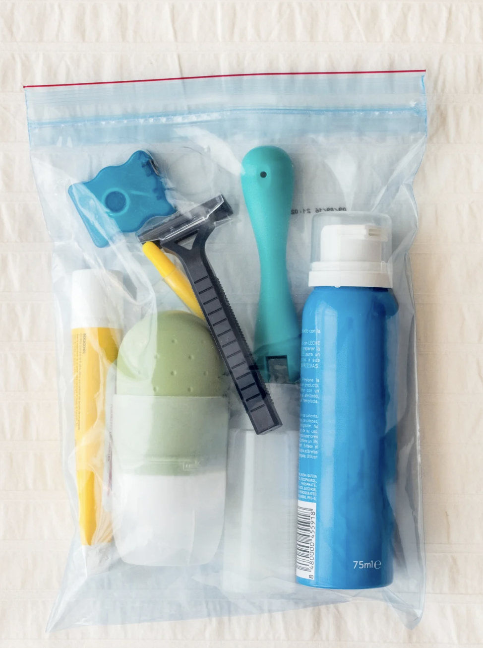 A resealable plastic bag containing a yellow razor, a blue shaver, a blue spray bottle, a green egg-shaped container, and a small blue and yellow plastic item.