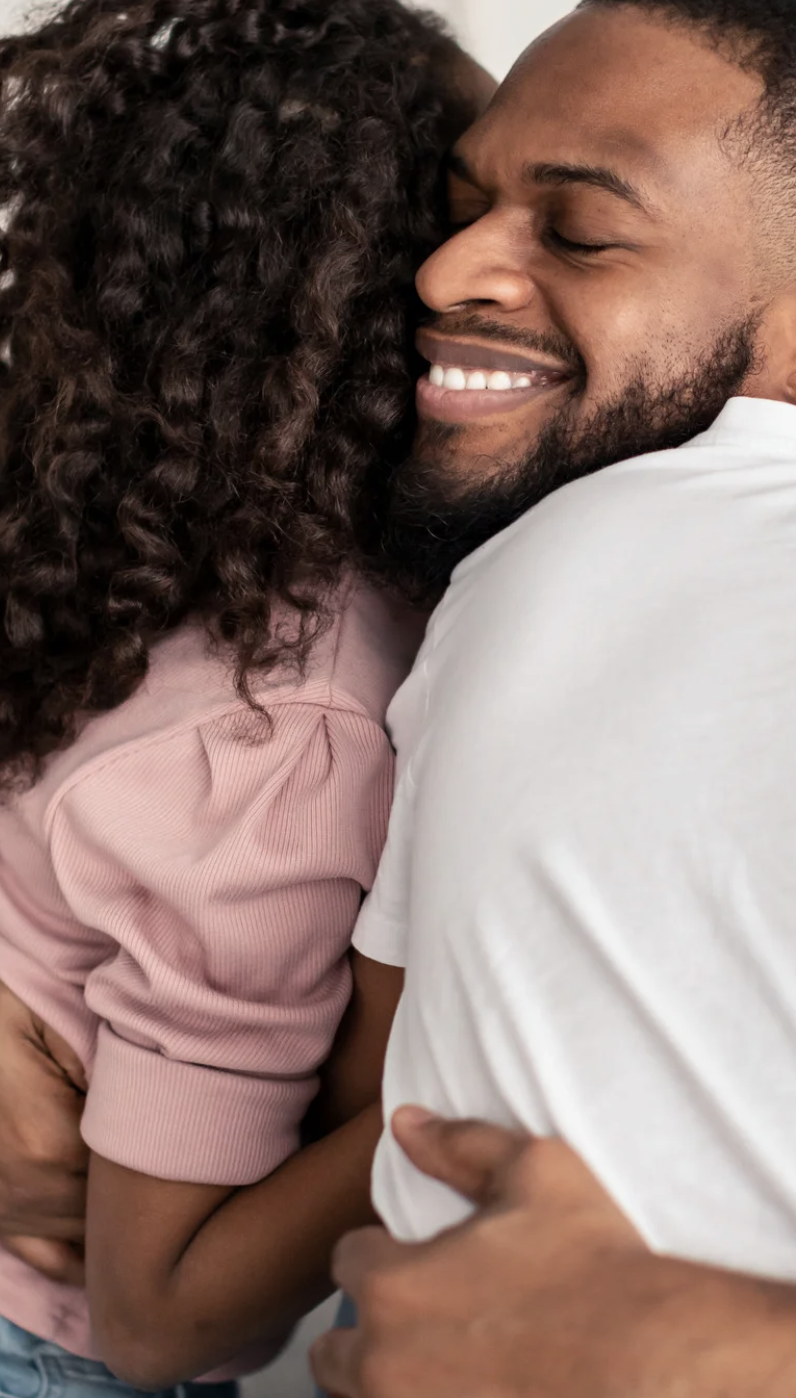 A man and a woman sharing a warm hug, with the man's eyes closed and smiling.