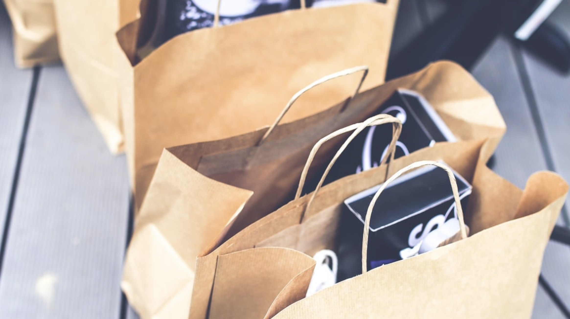Multiple paper shopping bags with black, brown, and tan paper bags, some with twisted paper handles, arranged on a table or surface.