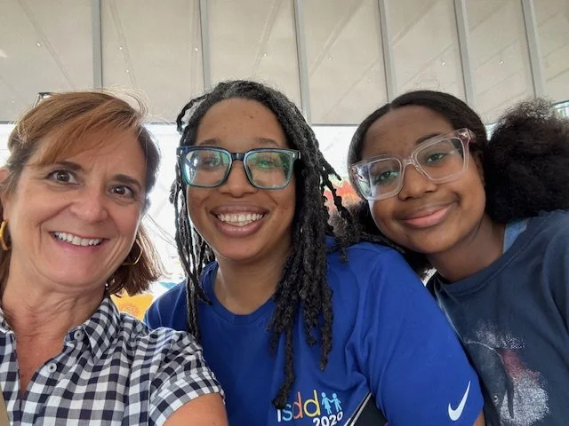 Three women smiling for a selfie in an indoor setting with glass walls.