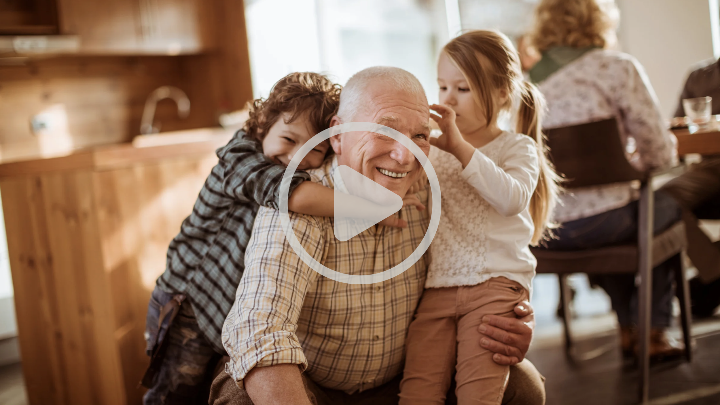An elderly man with children smiling and hugging him in a kitchen.