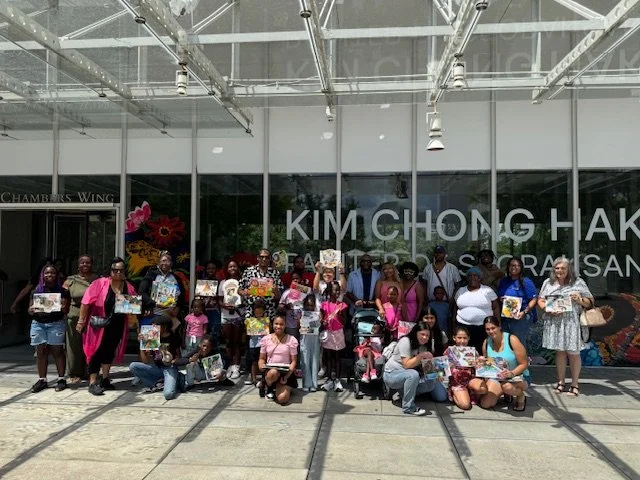 Group of children and adults holding books and standing in front of the Kim Chong Hak Museum or library.