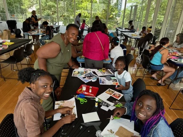 Children and adults participating in arts and crafts activities in a bright, spacious room with large windows and greenery outside.