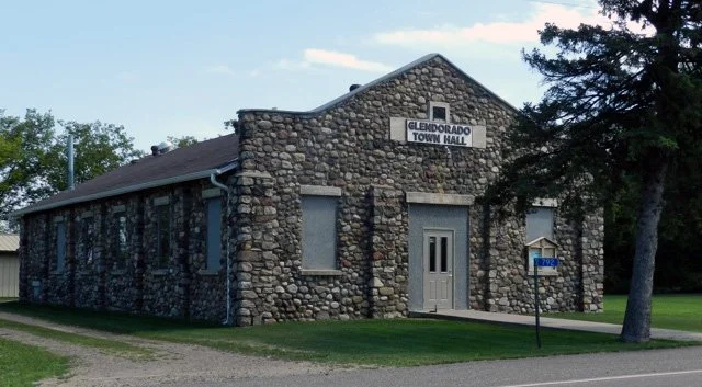 Stone building with a sign that reads "Gledorado Town Hall," a door, windows, and a street sign in front.