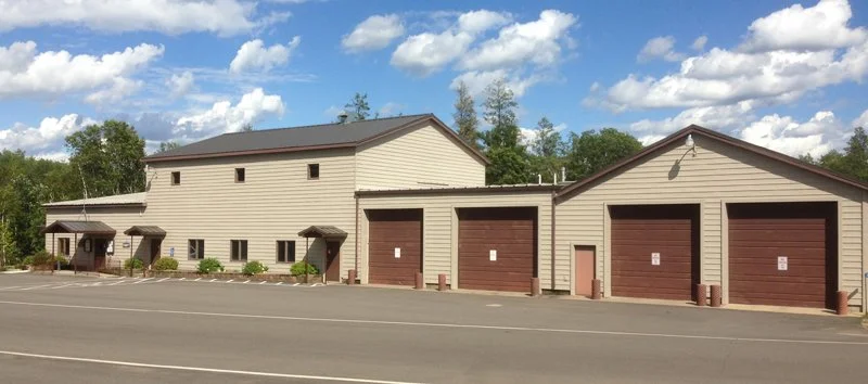 A light beige building with three garage doors, small covered entrances, and a few windows, under a partly cloudy sky.