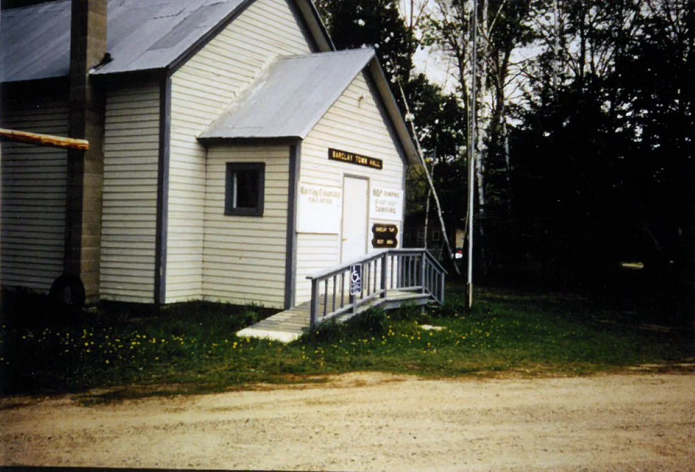 Small white church with a ramp and sign that reads "Island City Hall" in a grassy area with trees in the background.