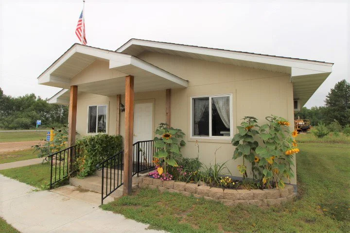 Small house with a covered porch, two windows, and a flower garden in front.