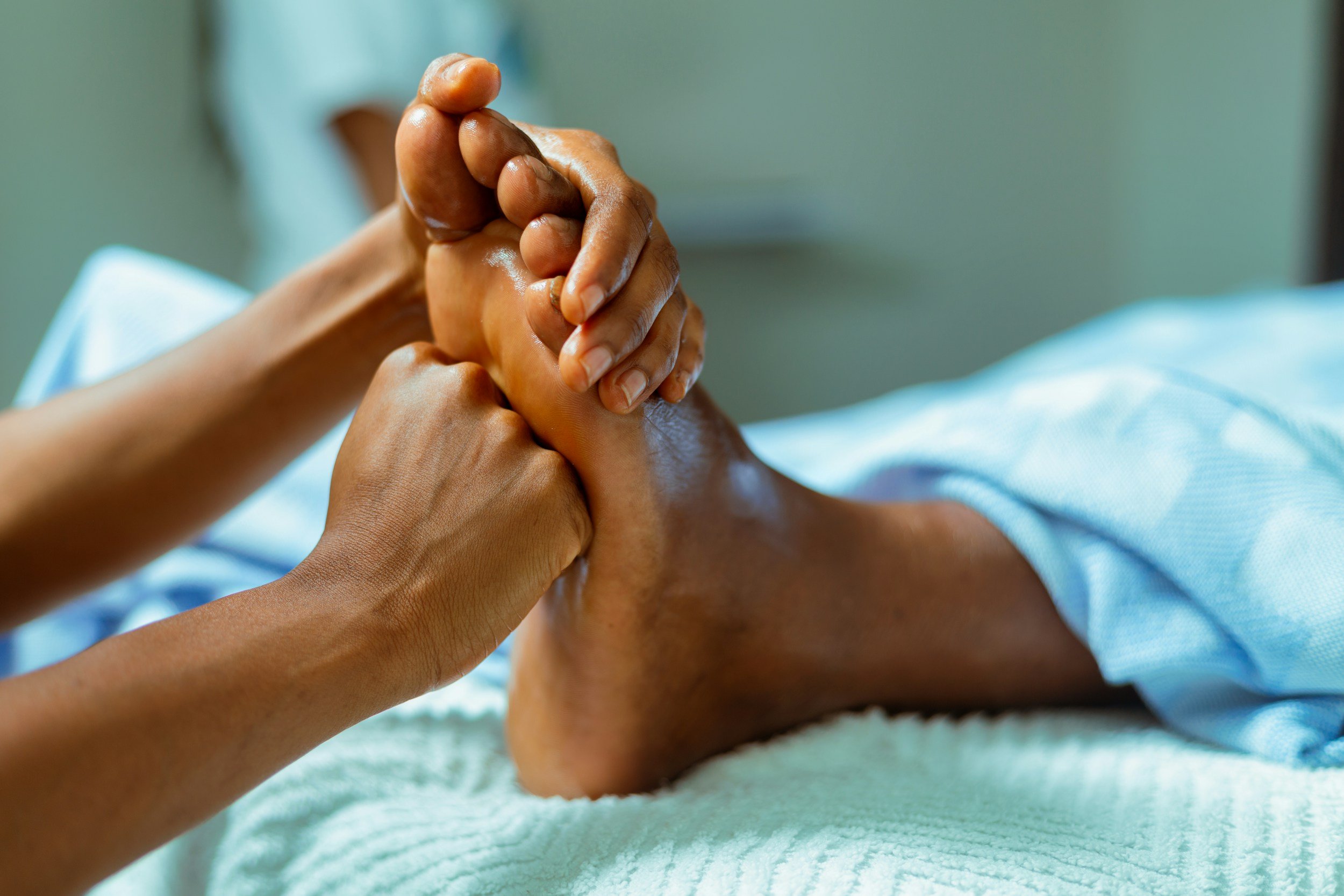 Close-up of a massage therapist's hands applying pressure on a person's leg during a massage, with focus on the hands and leg, soft lighting, and a blurred background.