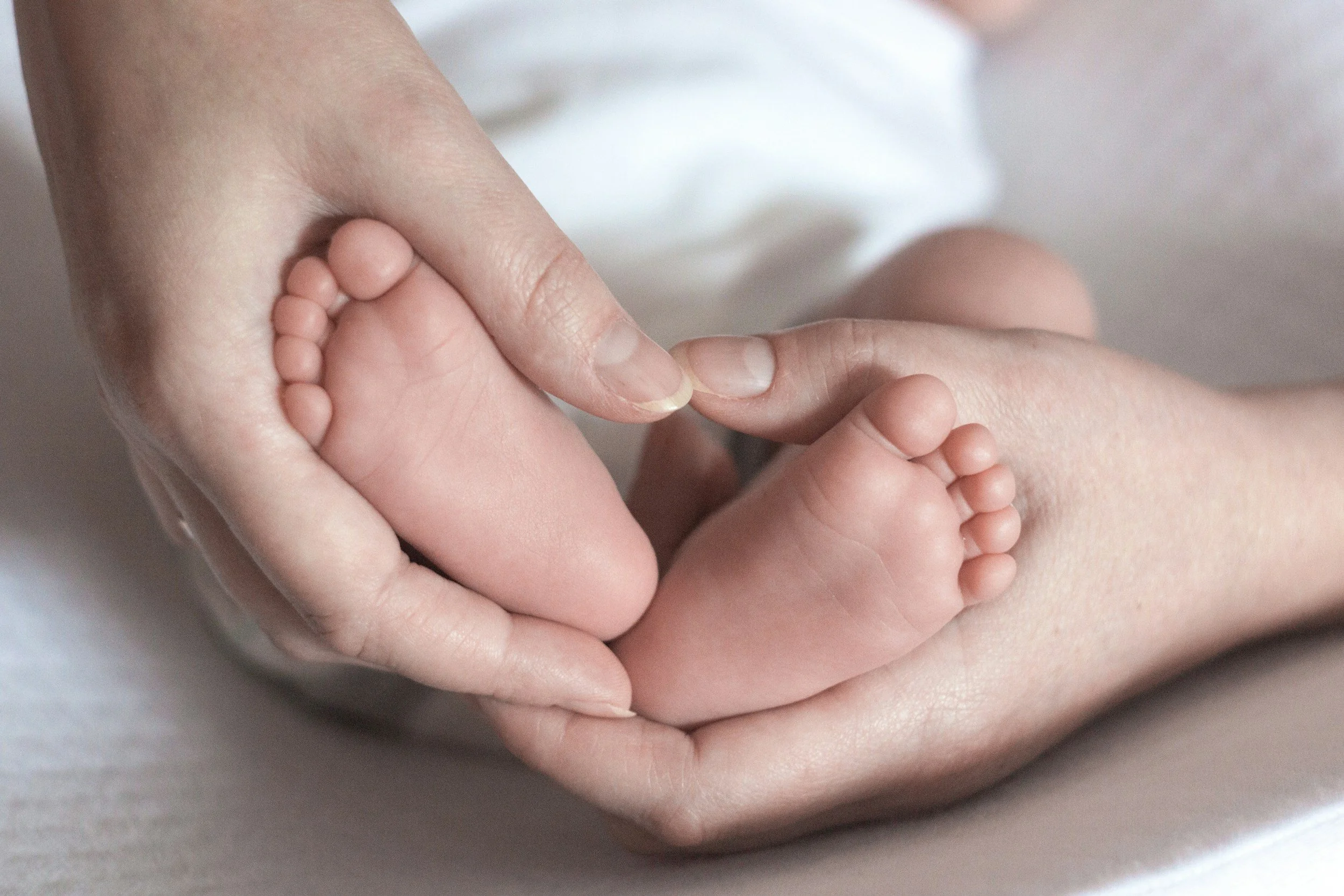Close-up of an adult's hand gently holding a baby's foot, showing the small toes and soft skin.