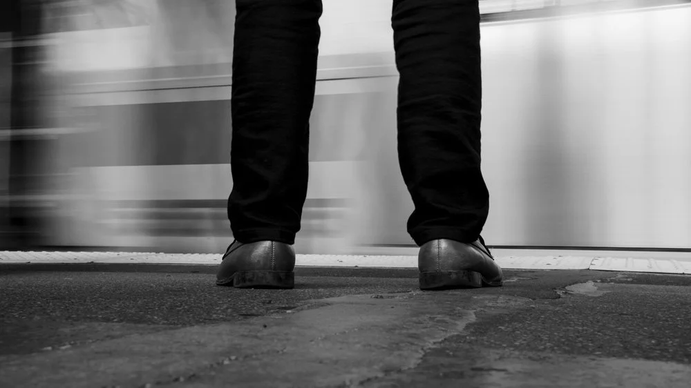 Person standing at subway station with train passing by in background.