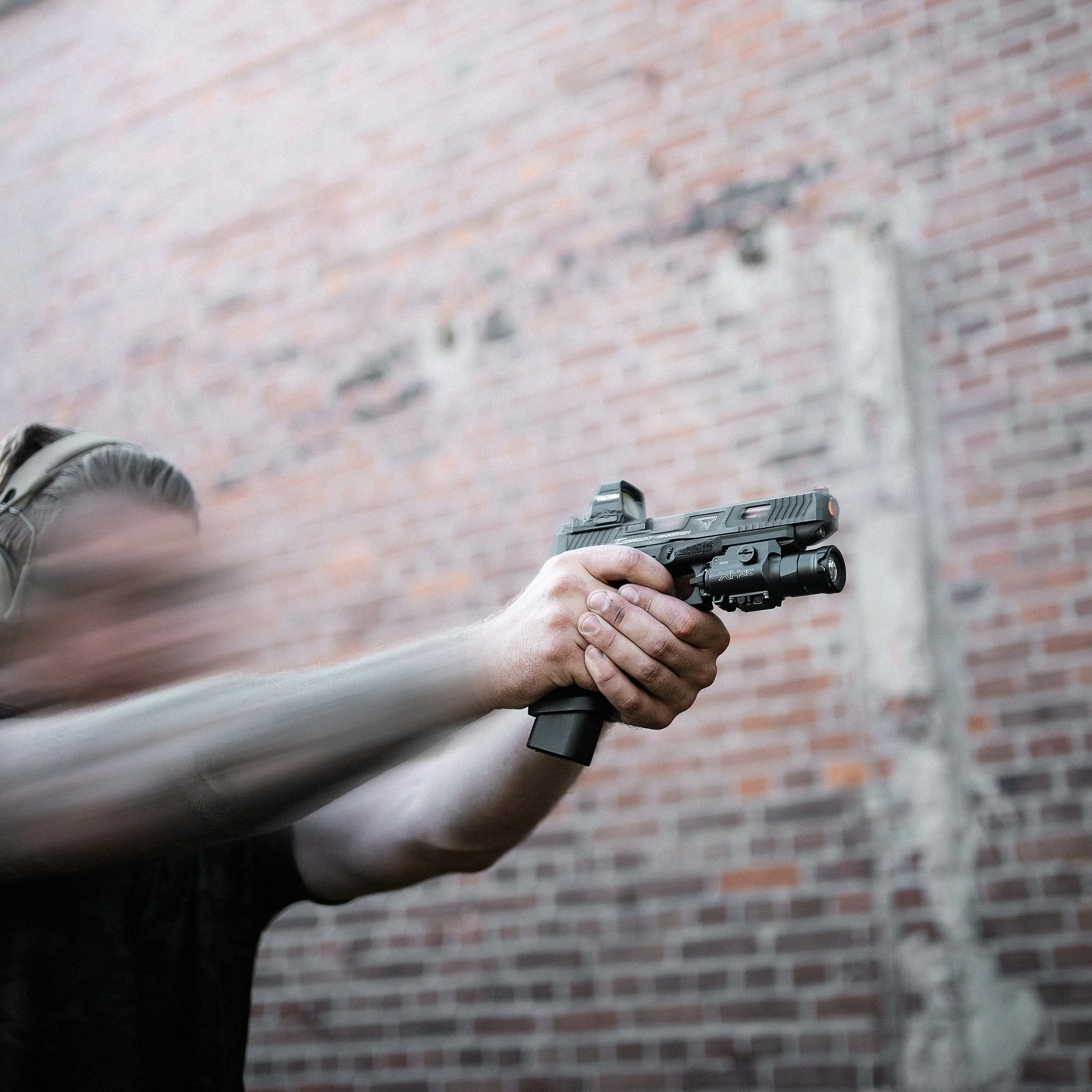 Person holding a semi-automatic pistol with both hands, aiming it forward against a brick wall background.