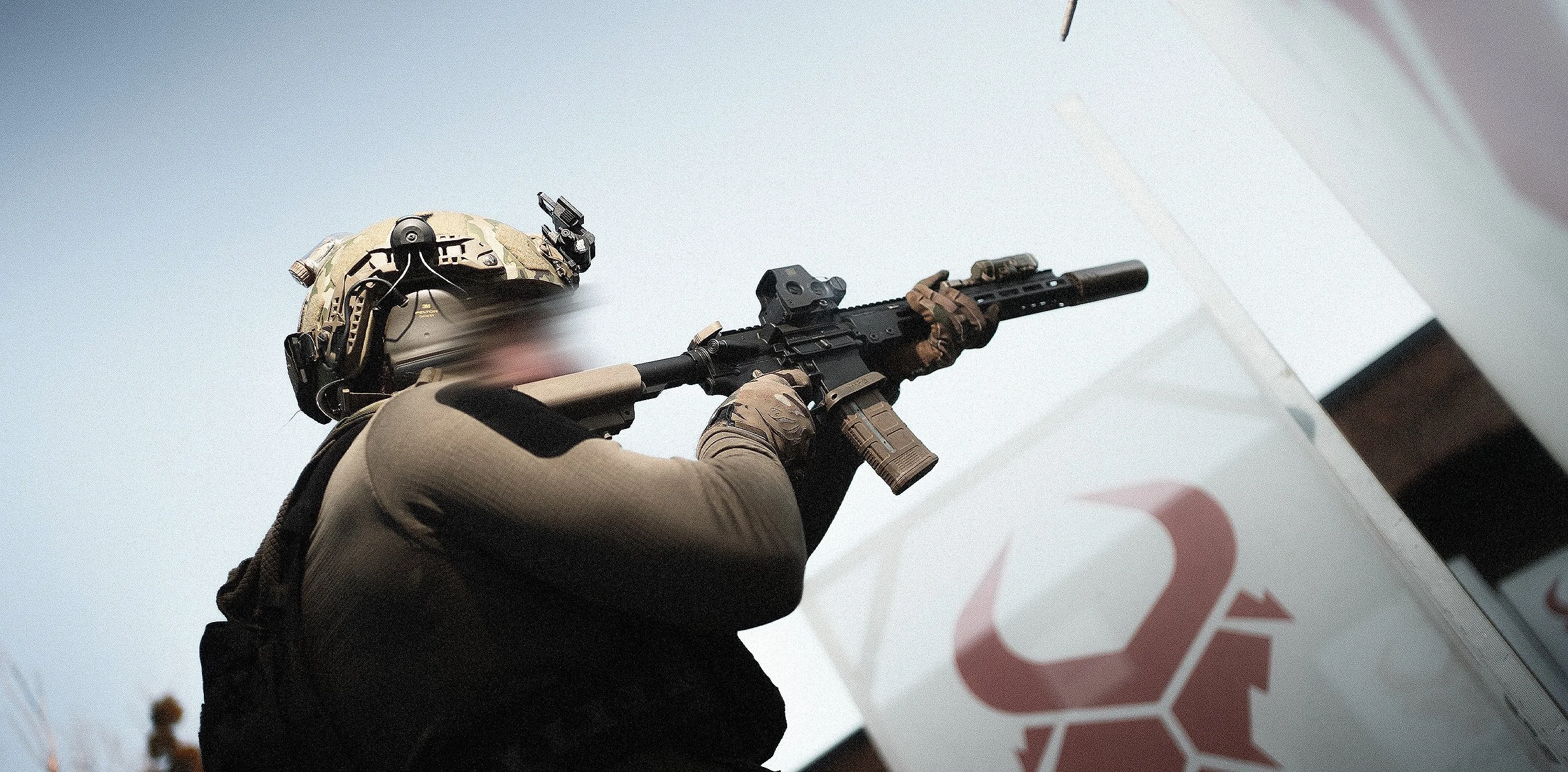 A soldier wearing tactical gear and a helmet aiming a rifle upwards.