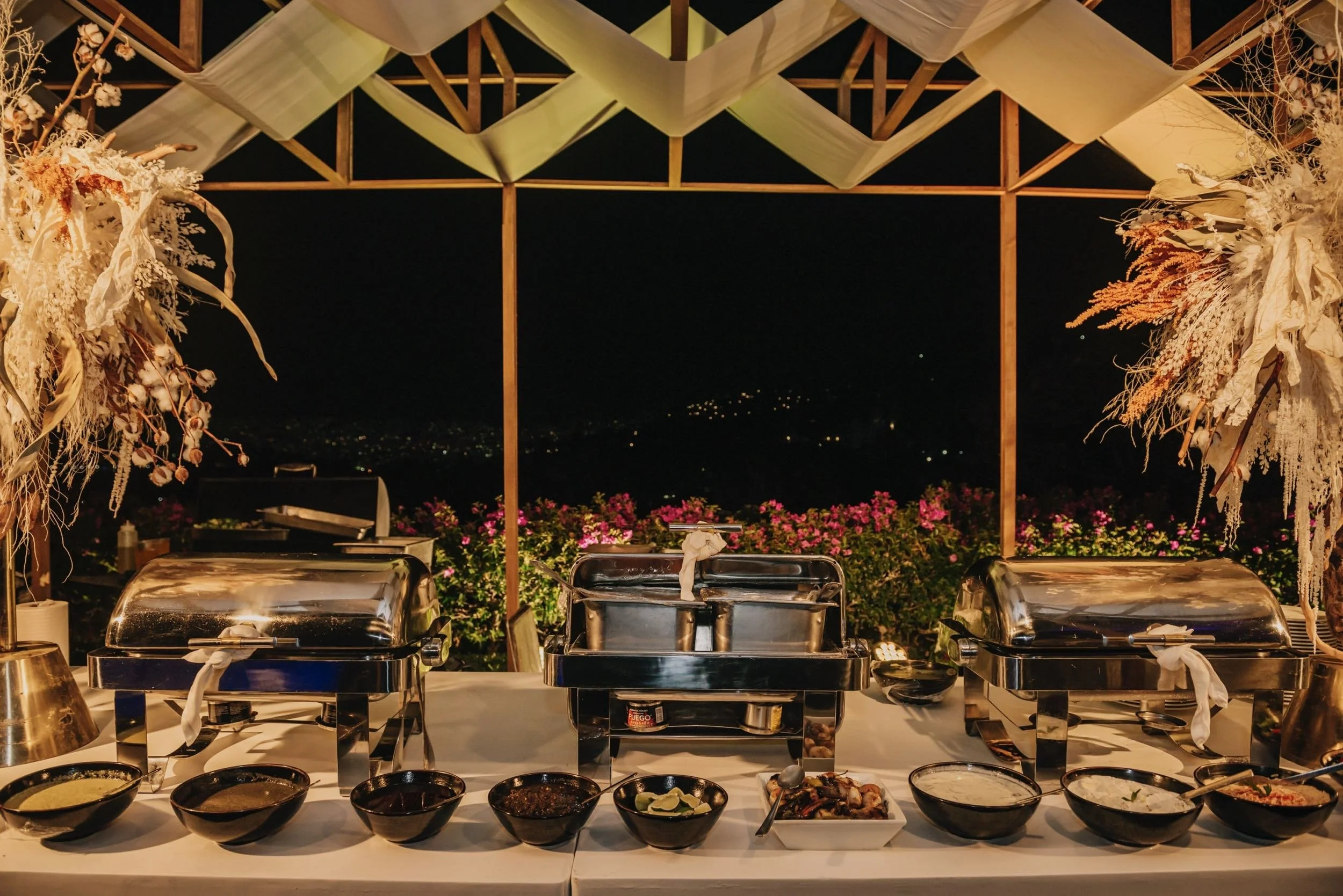 Estación de banquete nocturno iluminada en terrazas de Hotel Encanto Acapulco. Una celebración guiada por la acústica.