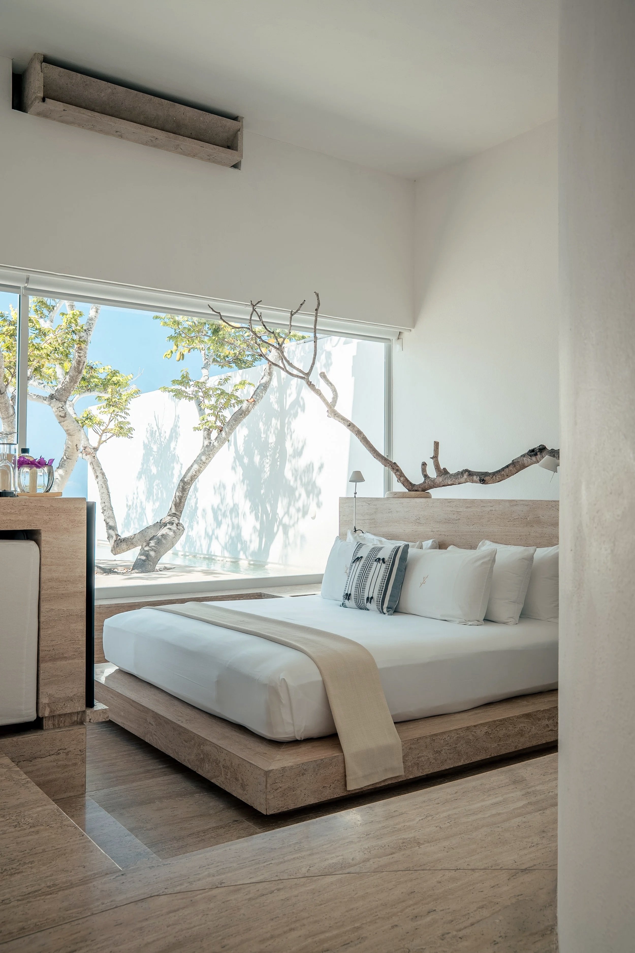 Habitación de concreto blanco y travertino abierta al paisaje en Hotel Encanto. Integración de la escala humana.