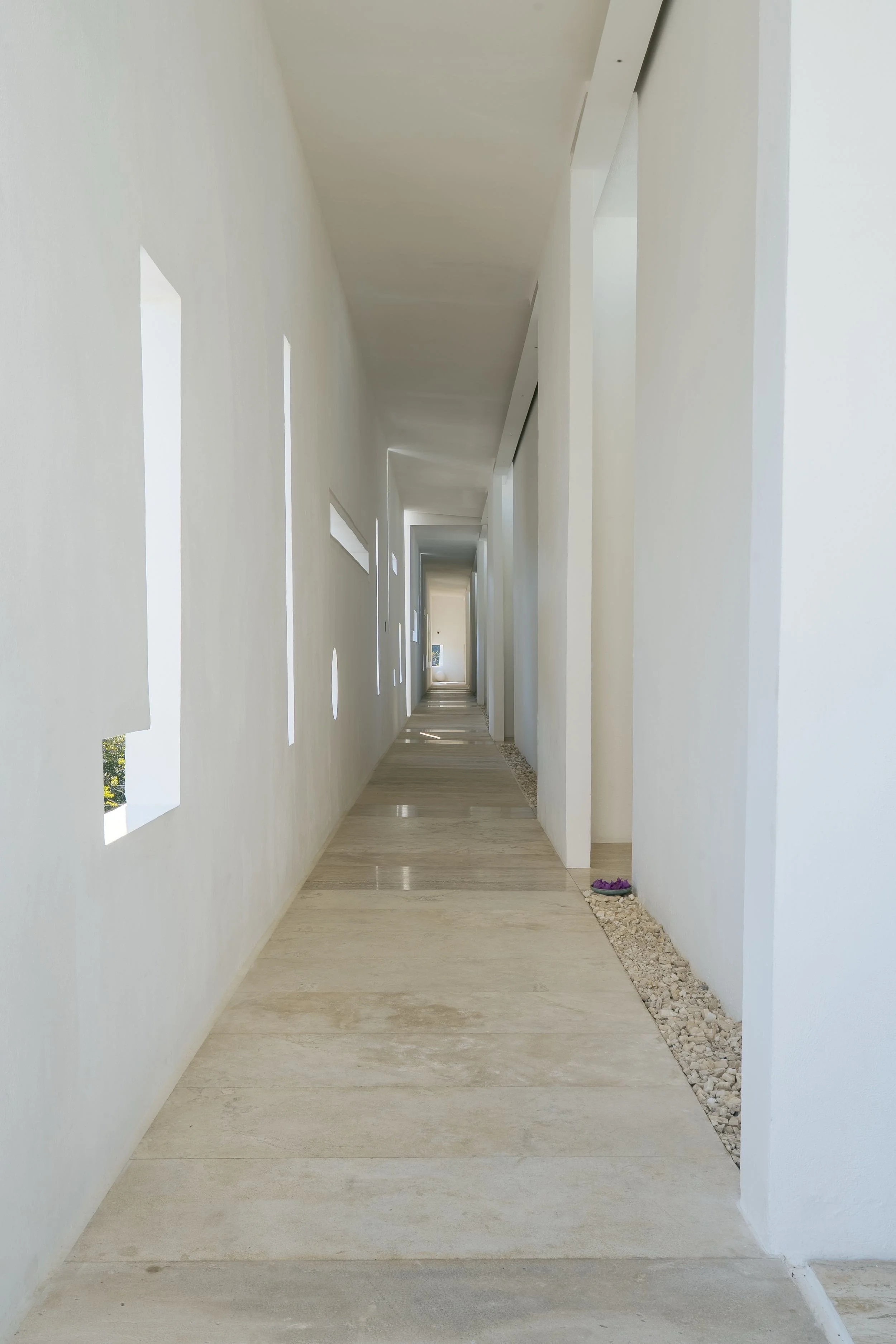 Corredor de líneas puras con ventanas rectangulares, iluminación sutil y detalles de vegetación interna.