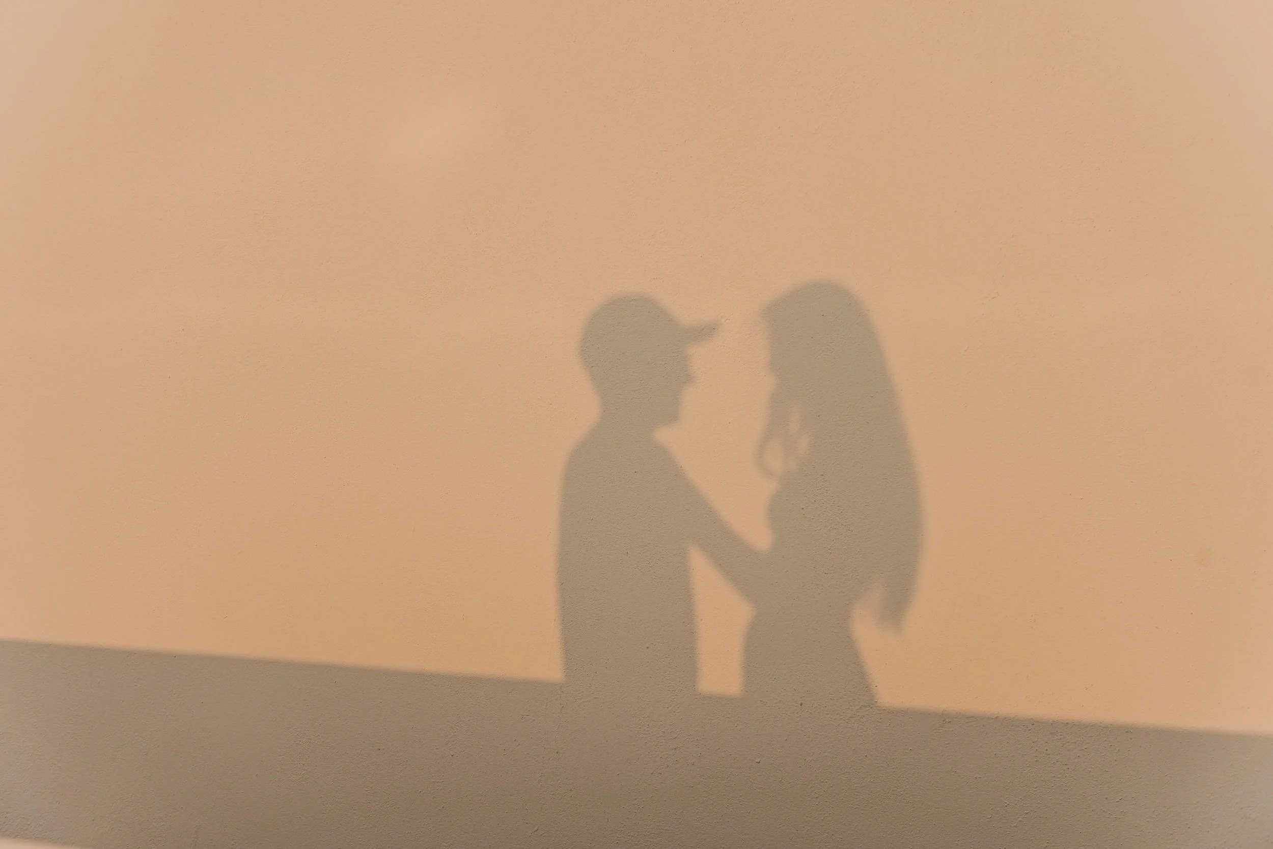 Sombras de novios proyectadas en muro blanco al atardecer en Hotel Encanto Acapulco. Juego de luces sutiles en la calma.