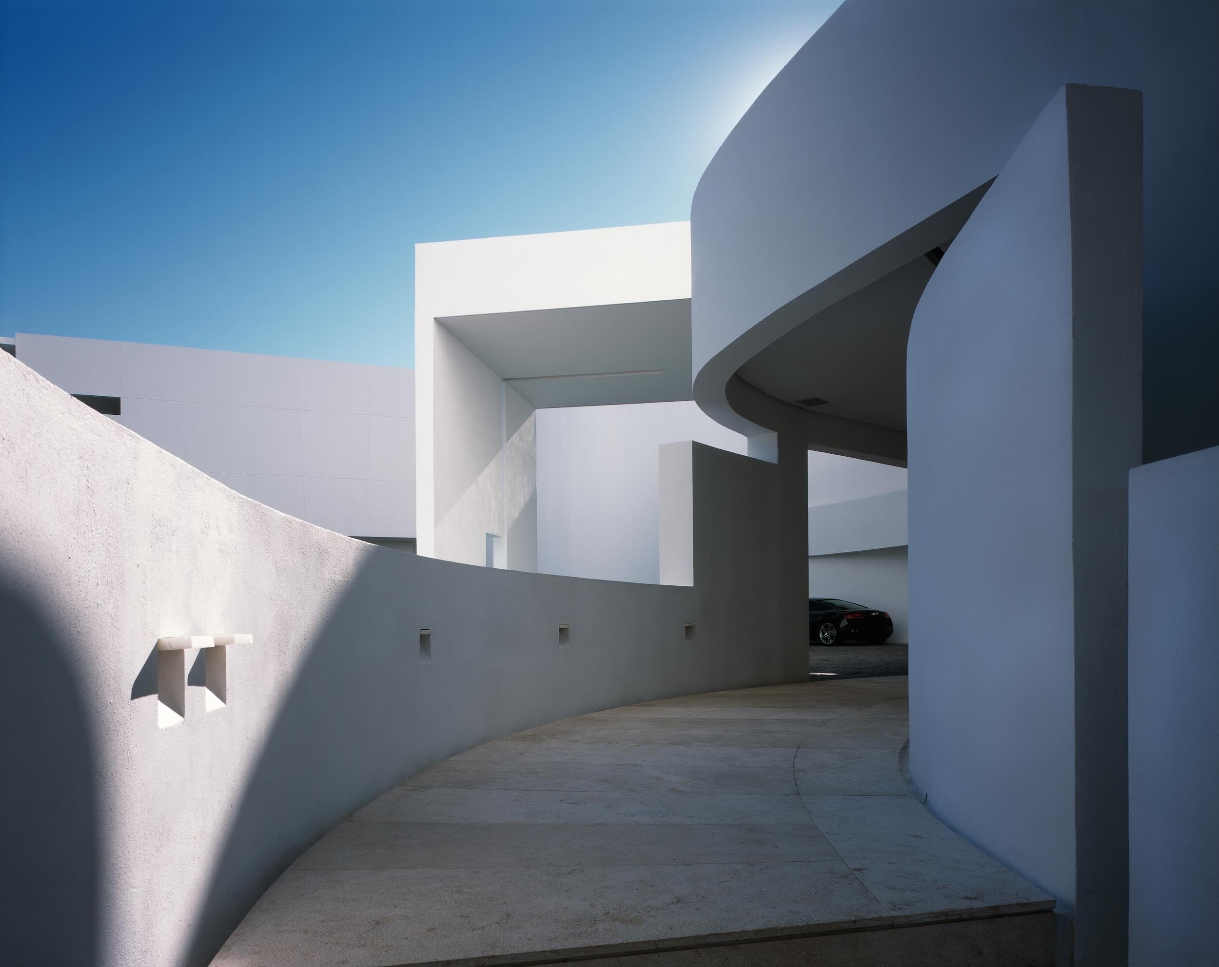 Arquitectura contemporánea de Miguel Ángel Aragonés en Hotel Encanto Acapulco. Fotografía de Joe Fletcher. Pasillo exterior con muros curvos blancos y cielo azul de fondo. 