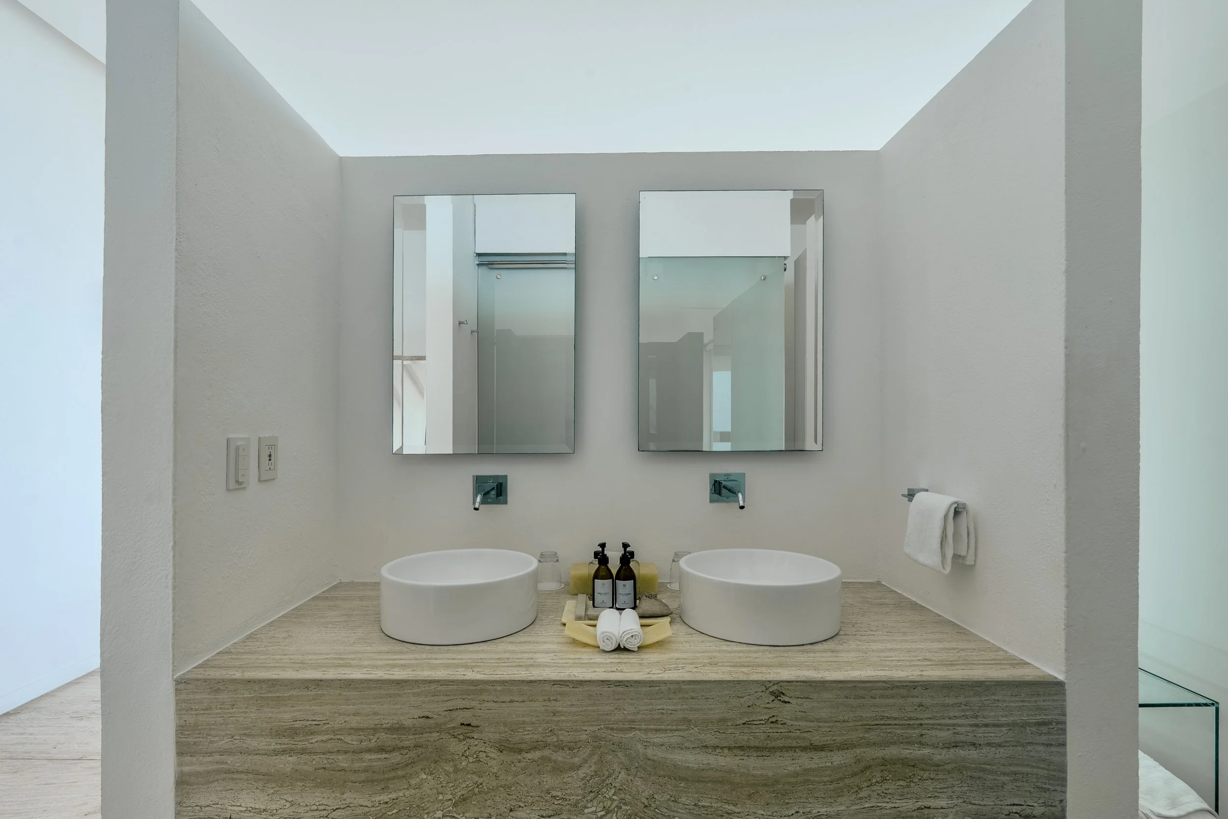 Baño minimalista de mármol con doble lavabo y espejos iluminados en suite de diseño de Hotel Encanto Acapulco.