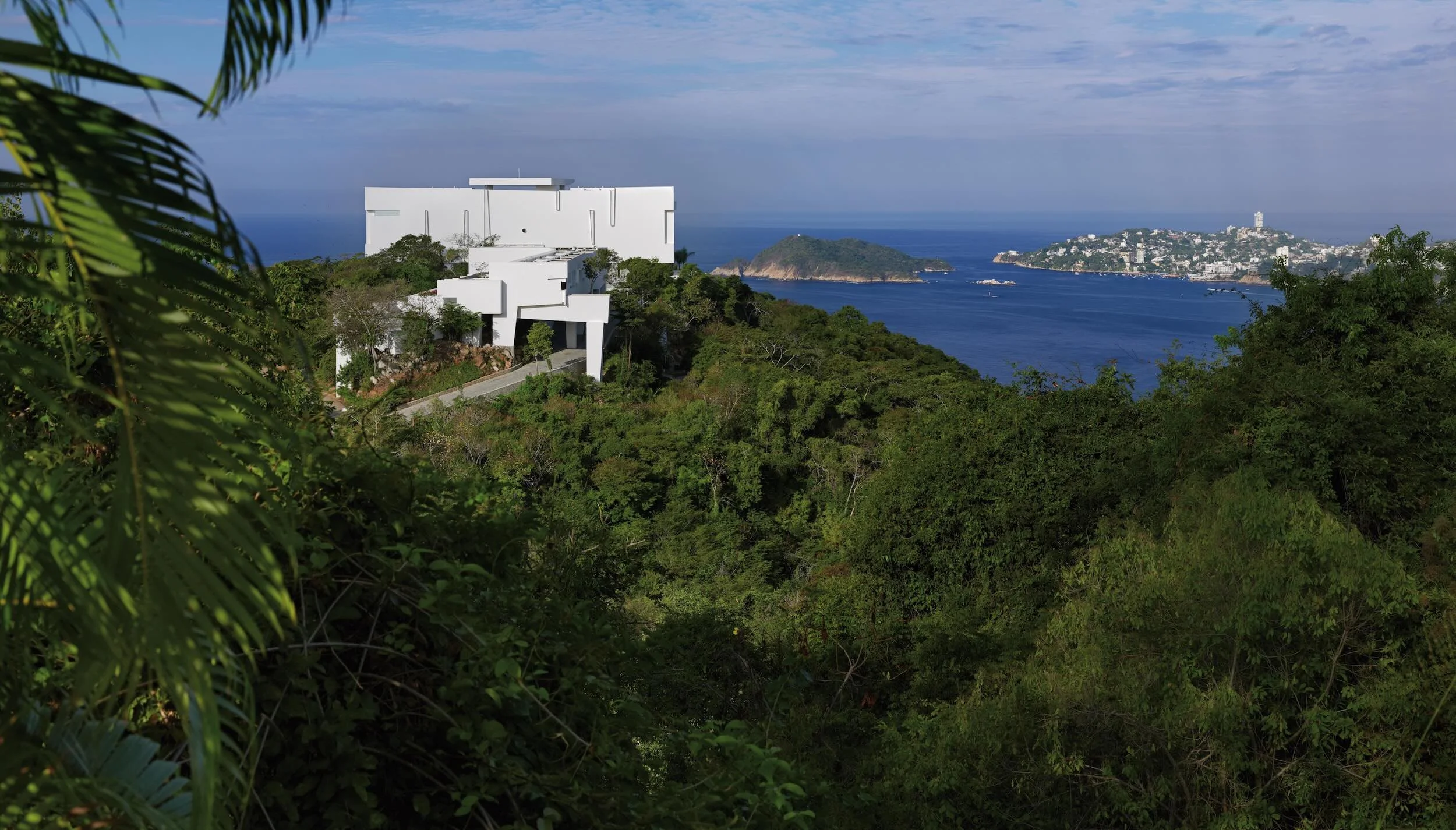 Arquitectura contemporánea de Miguel Ángel Aragonés en Hotel Encanto Acapulco. Fotografía de Joe Fletcher. Vegetacion abundante rodeando una estructura blanca.