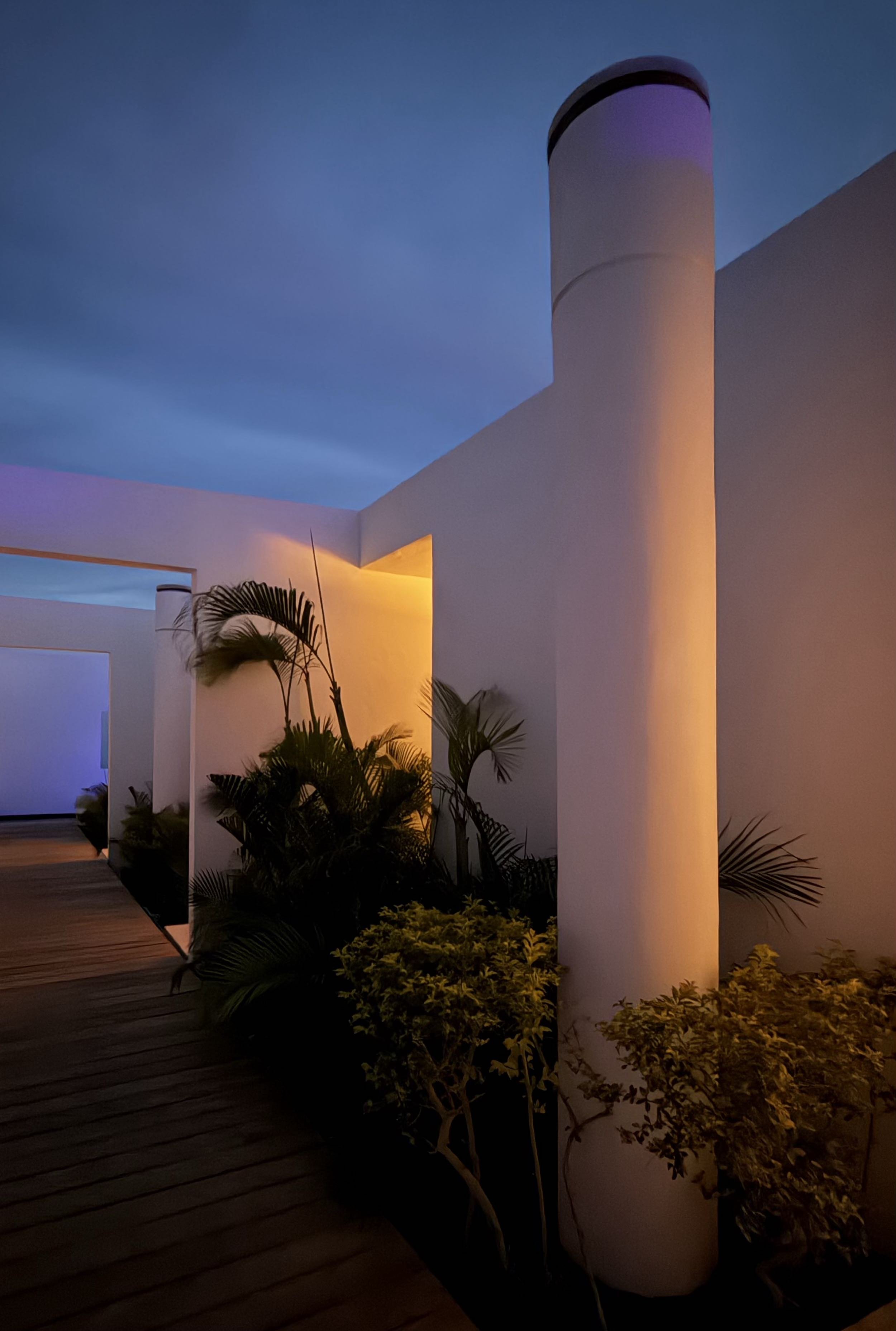 Pasillo de Acceso con iluminación calida de Signature Suite en Hotel Encanto. Vegetación tropical y cielo azul de fondo