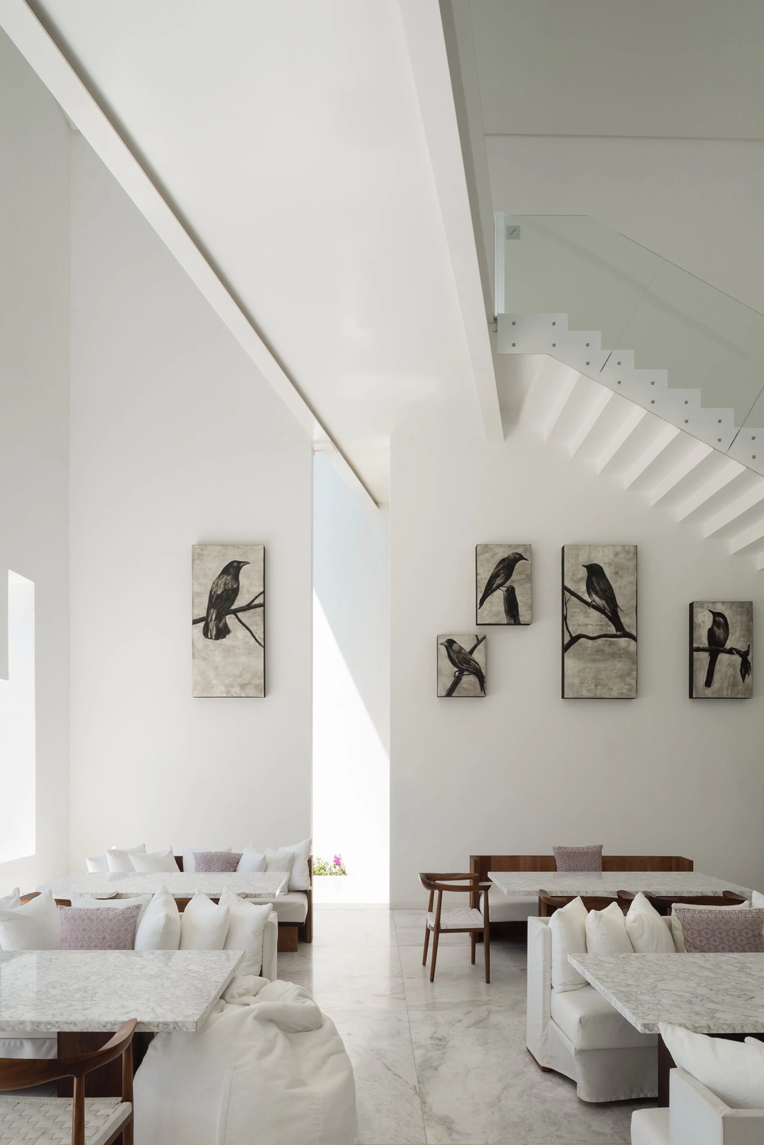Espacio interior de escala humana con altos muros monolíticos blancos, iluminación natural oblicua y mobiliario.