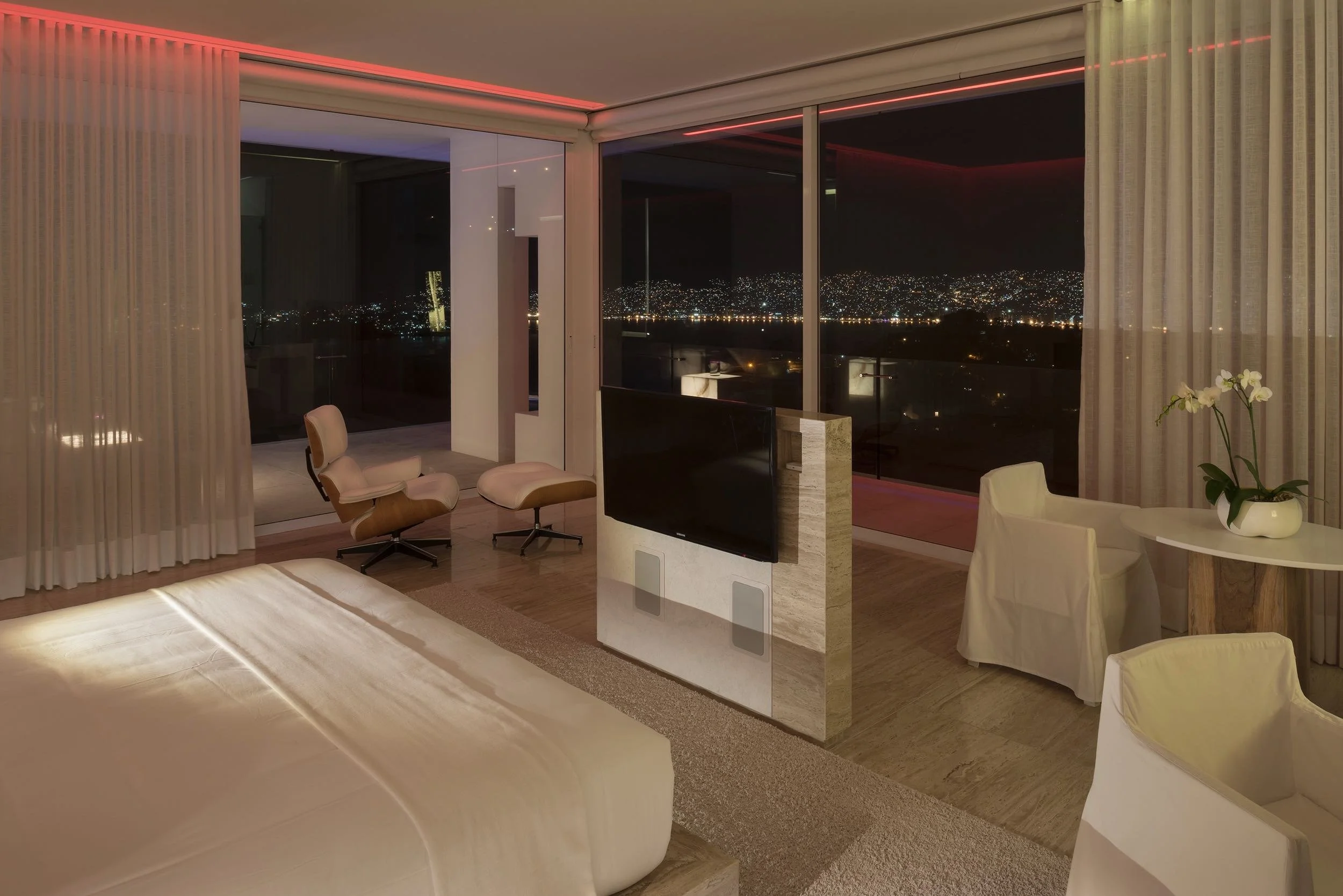 Experiencia cromática nocturna en la Ocean Designer Suite de Hotel Encanto. Ventanales hacia las luces de Acapulco.