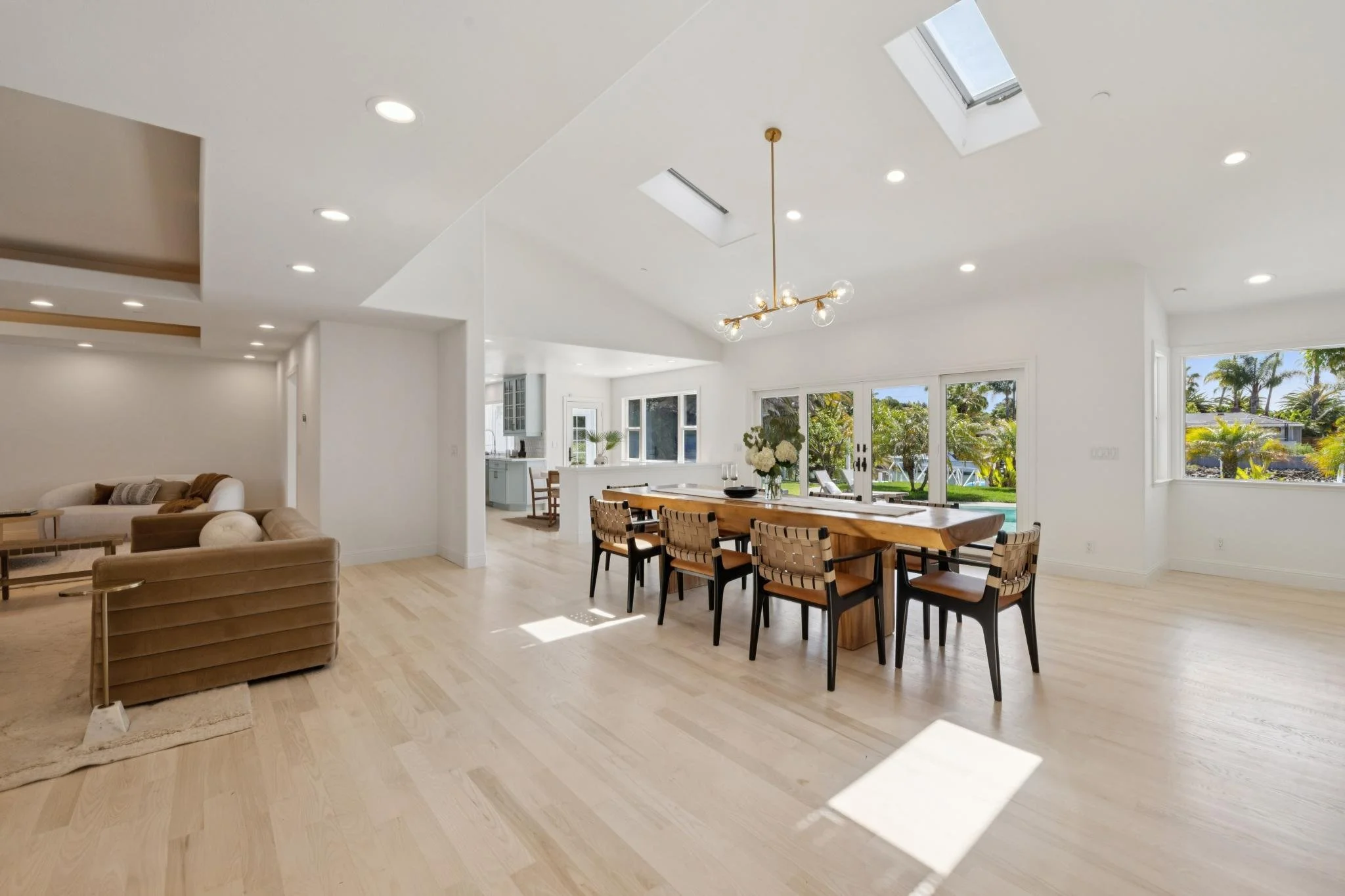 Bright open-concept living and dining area with large windows, skylights, and modern furnishings.