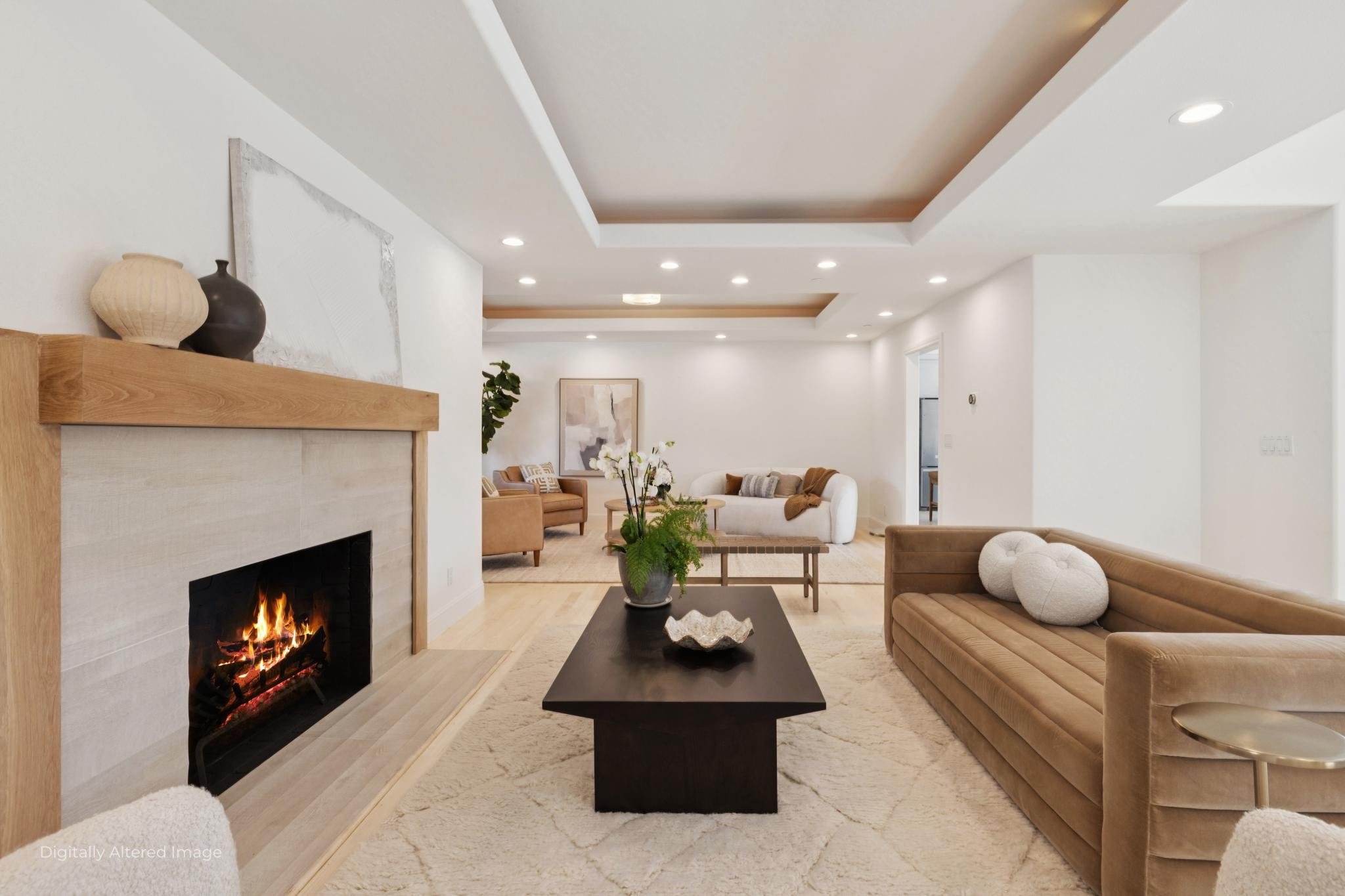 Modern living room with a fireplace, beige sofas, and a black coffee table decorated with a potted plant. Recessed ceiling lights and a large framed artwork on the wall add to the contemporary decor.