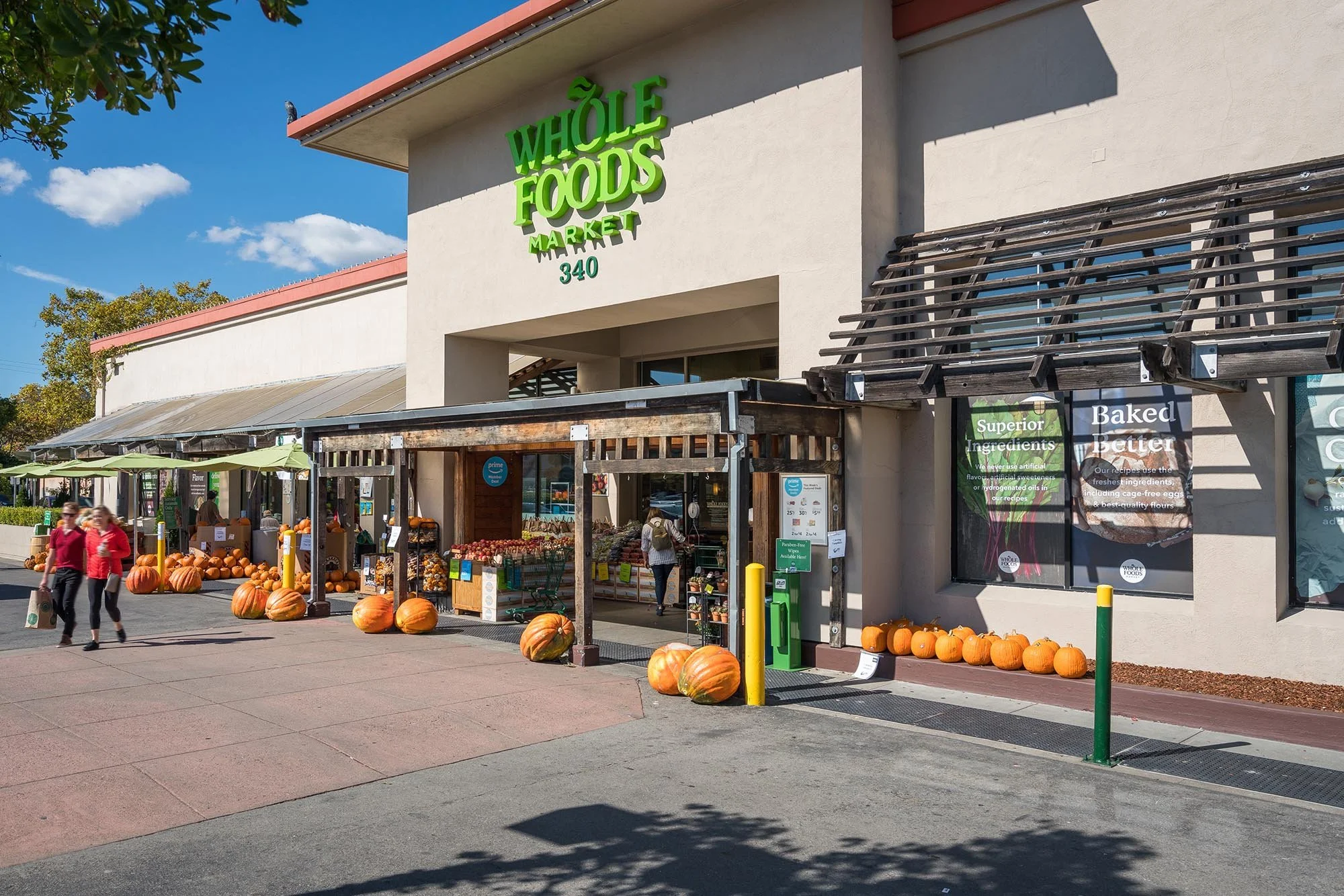 Exterior view of Whole Foods Market with pumpkin display outside, showing pumpkins lined up and shopping for pumpkins on a sunny day.
