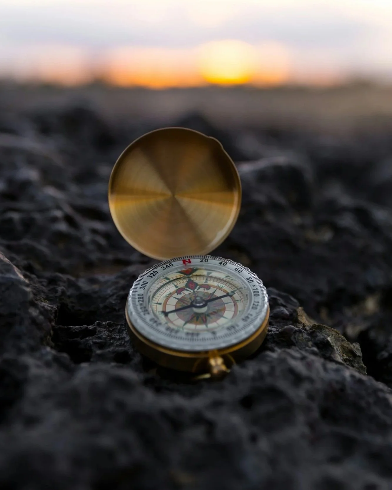 Vintage compass on volcanic rocks at sunset — representing clarity and direction, the foundation of Partner With Kate