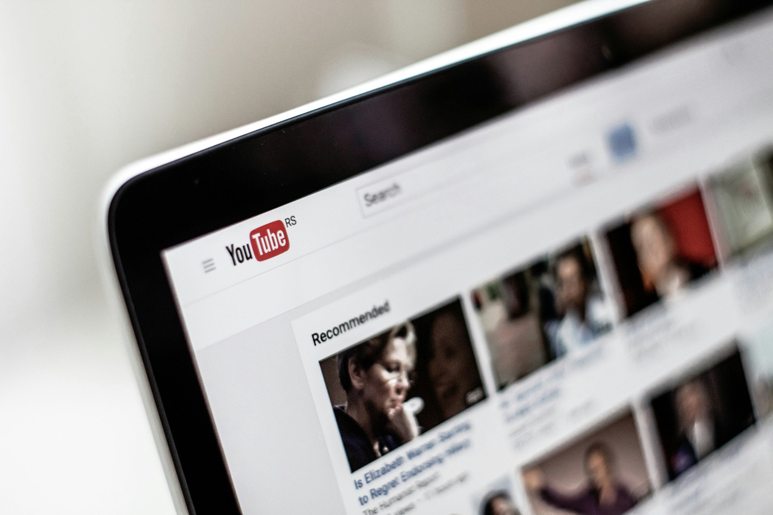 Close-up of a tablet screen displaying the YouTube homepage with various video thumbnails and the red YouTube logo at the top left.