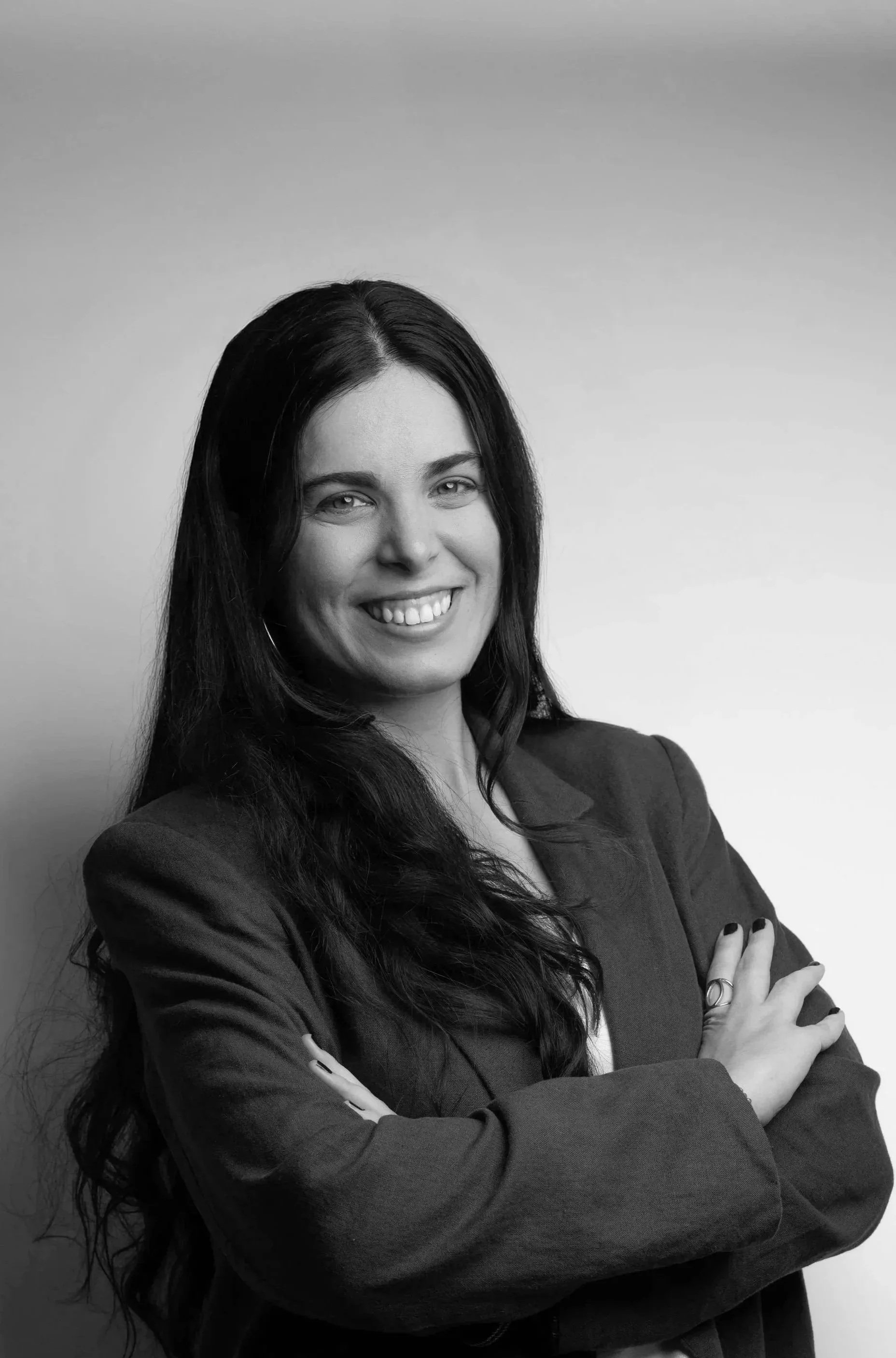 Black and white photo of a woman with long dark hair, smiling, outdoors with blurred trees in the background.
