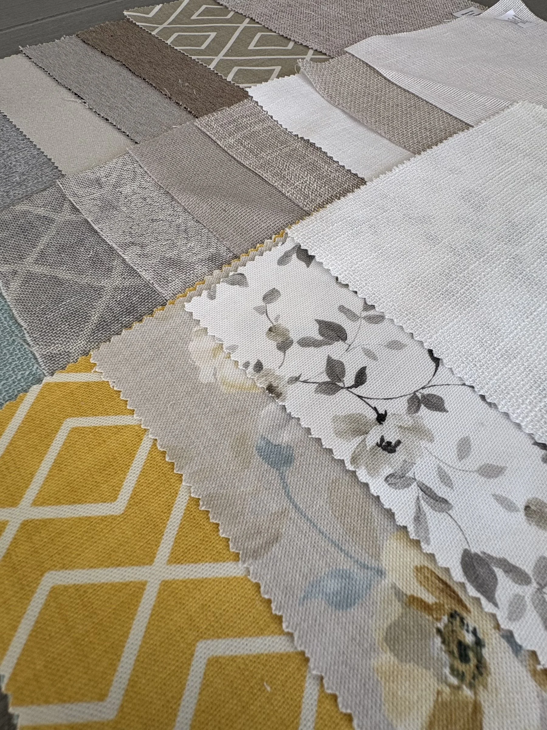 A collection of fabric swatches in various neutral shades and patterns, placed on a yellow patterned surface.