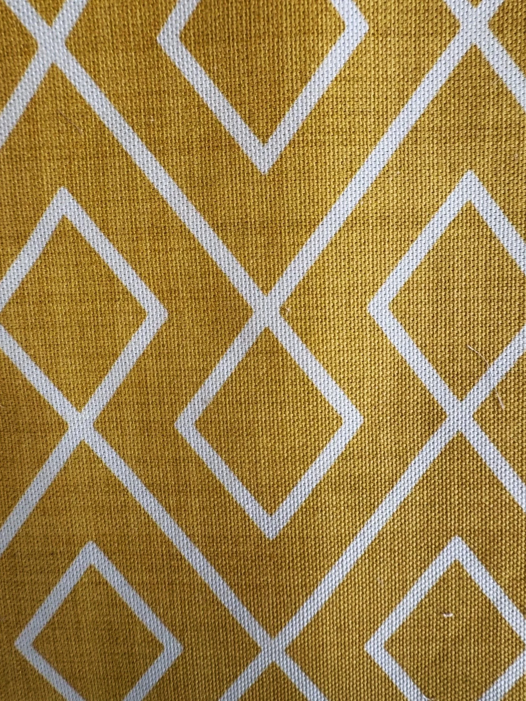Close-up of a yellow fabric with a white geometric diamond pattern.