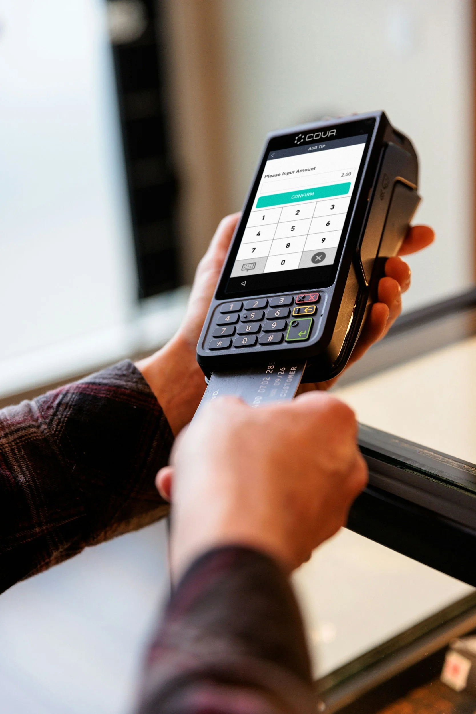 Close-up of a person holding a handheld point-of-sale credit card terminal with a receipt card inserted, pressing buttons to process a payment.