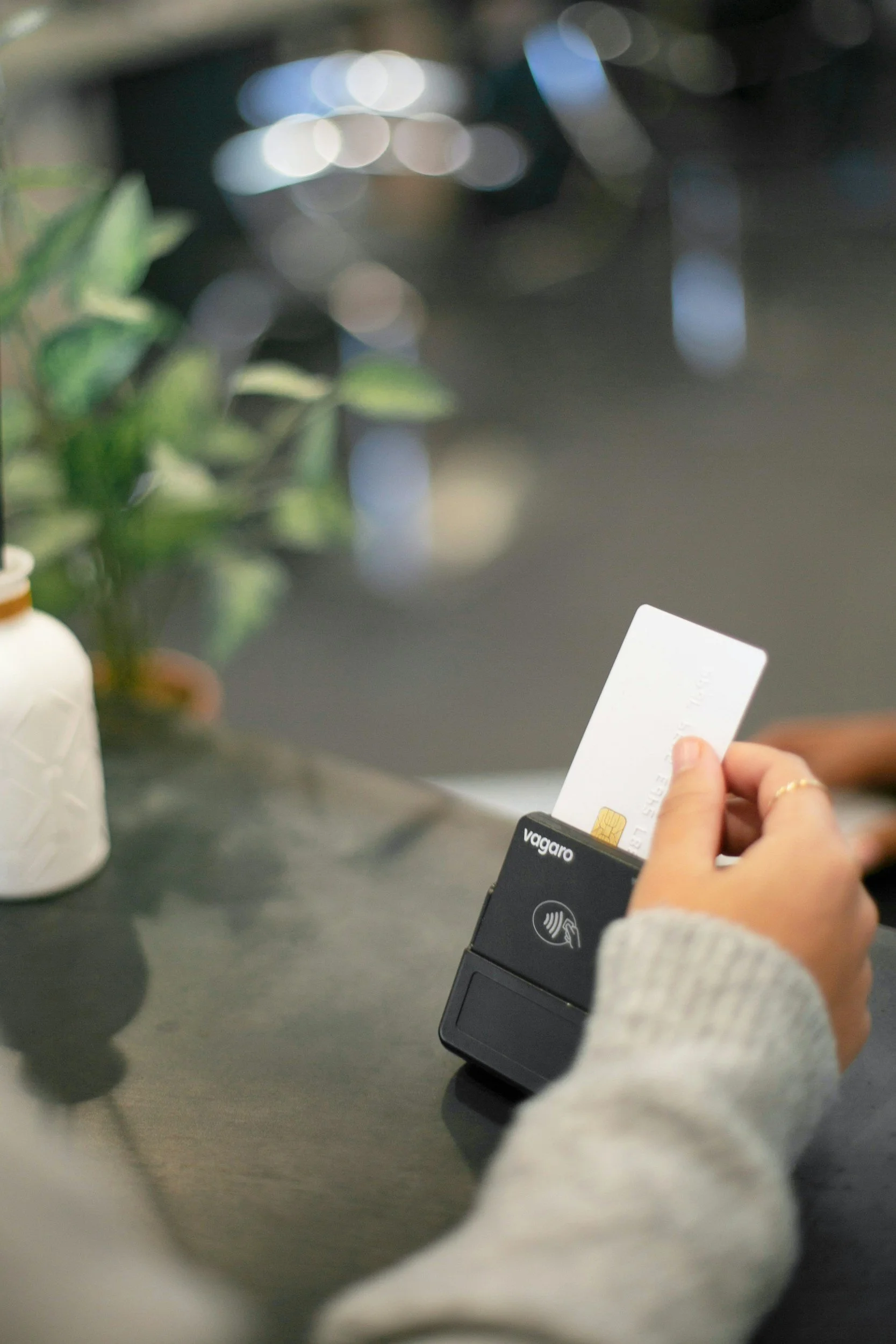 A person holding a credit card and a white card, using a contactless payment terminal.