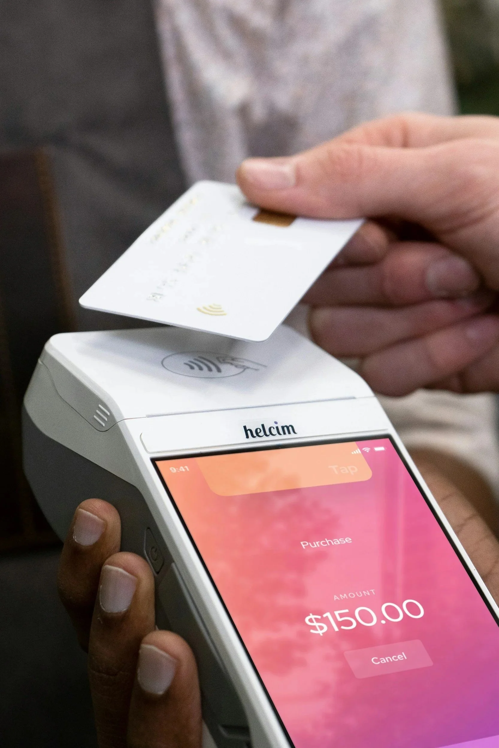 Close-up of a person holding a white payment terminal with a smartphone screen showing a digital payment confirmation of $150.00, and inserting a contactless credit card into the terminal.