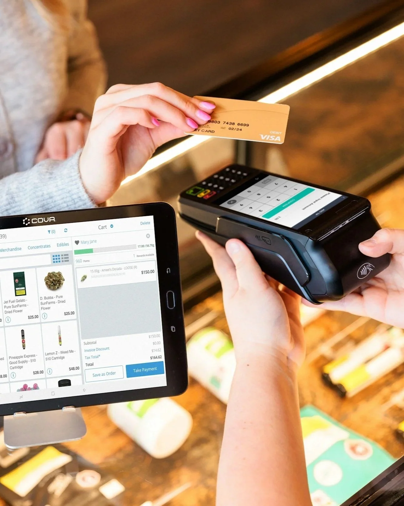 A person using a tablet and payment terminal to process a purchase at a store, with another person holding a yellow credit card.