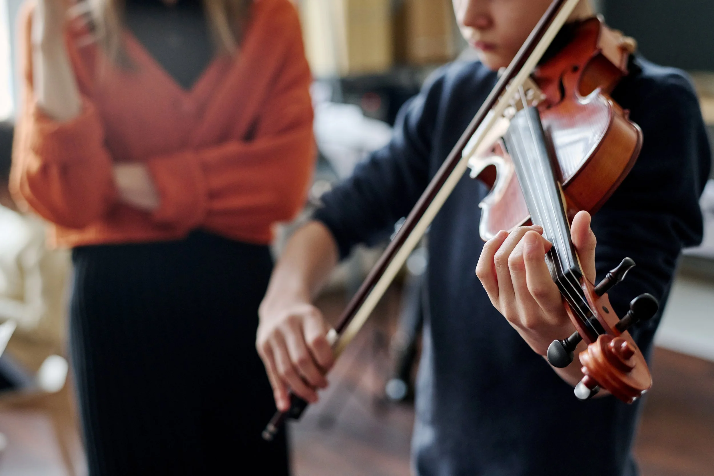 A person playing a violin with another person in the background, possibly giving a music lesson.