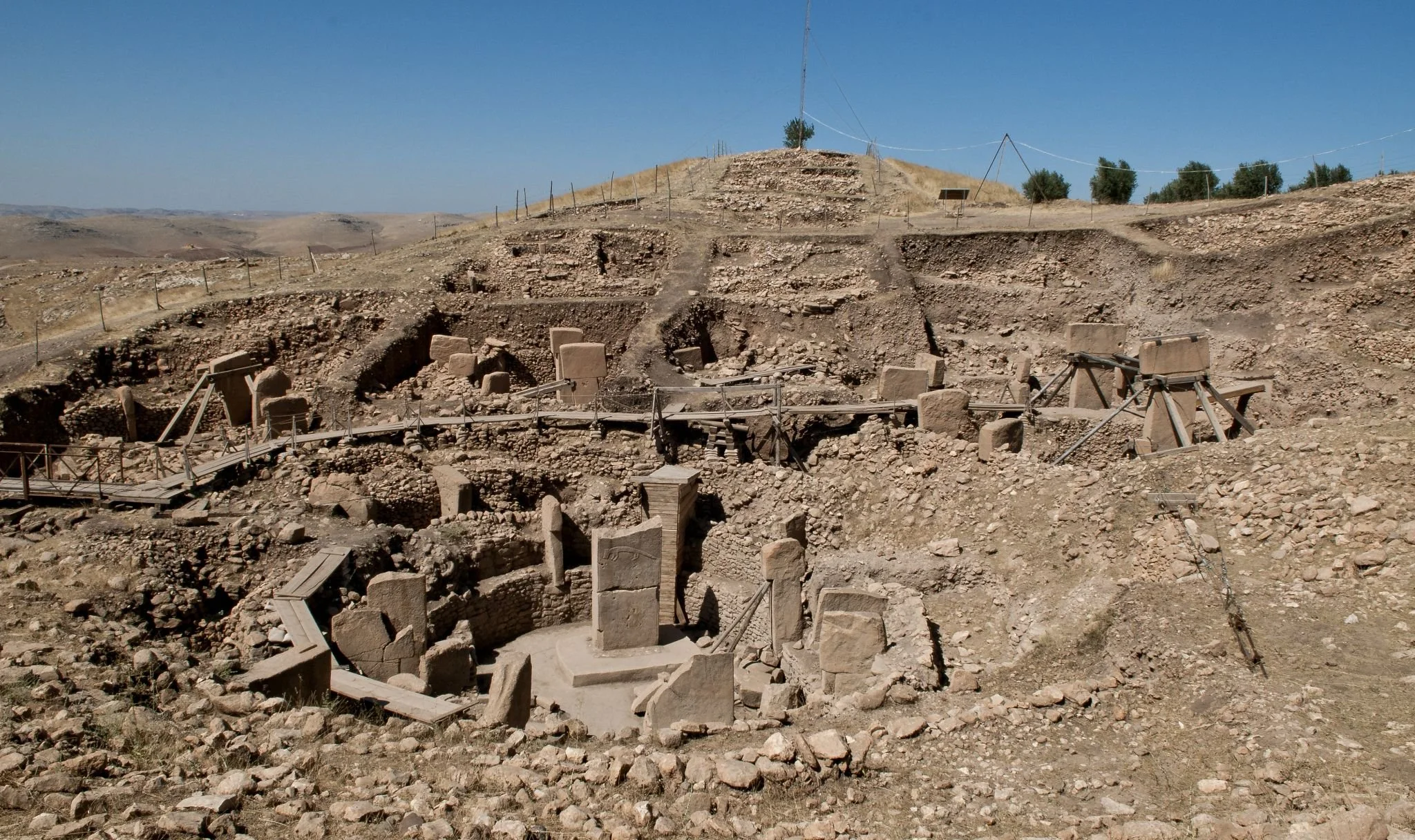 Archaeological excavation site with stone structures and ruins on a dry hillside under a clear blue sky.
