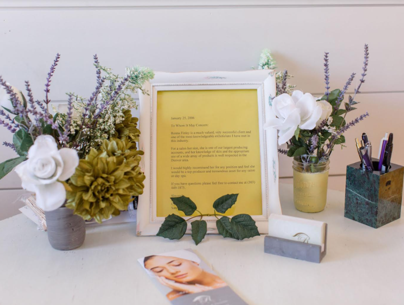 Decorative desk setup with various vases of flowers, a framed document, a business card holder, and a brochure on a white surface.
